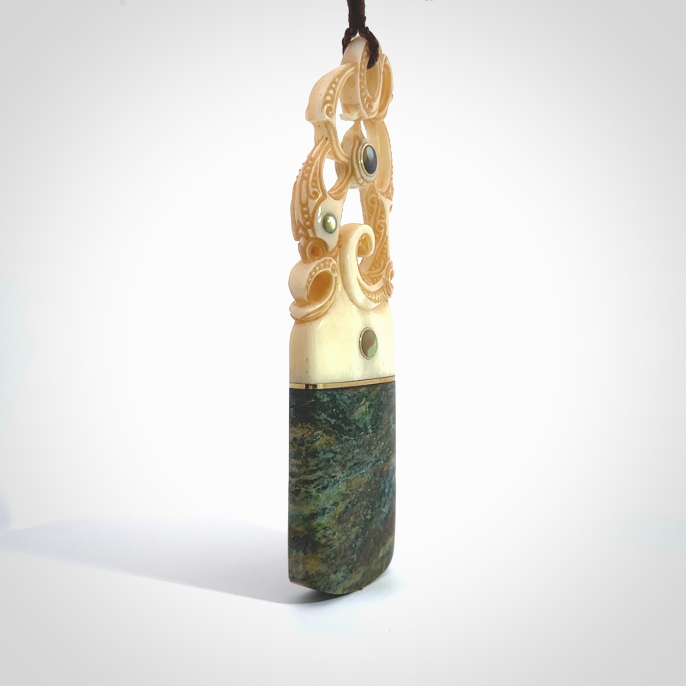 This is a large carved Manaia pendant. It is made from unique materials - New Zealand Obay Stone, Bone, Paua shell, Brass and Mother of Pearl. The face of the Manaia is carved with a traditional design in the front. It is carved front and back and has traditional carved designs. This is a large and very traditional pendant that is a collectors piece.