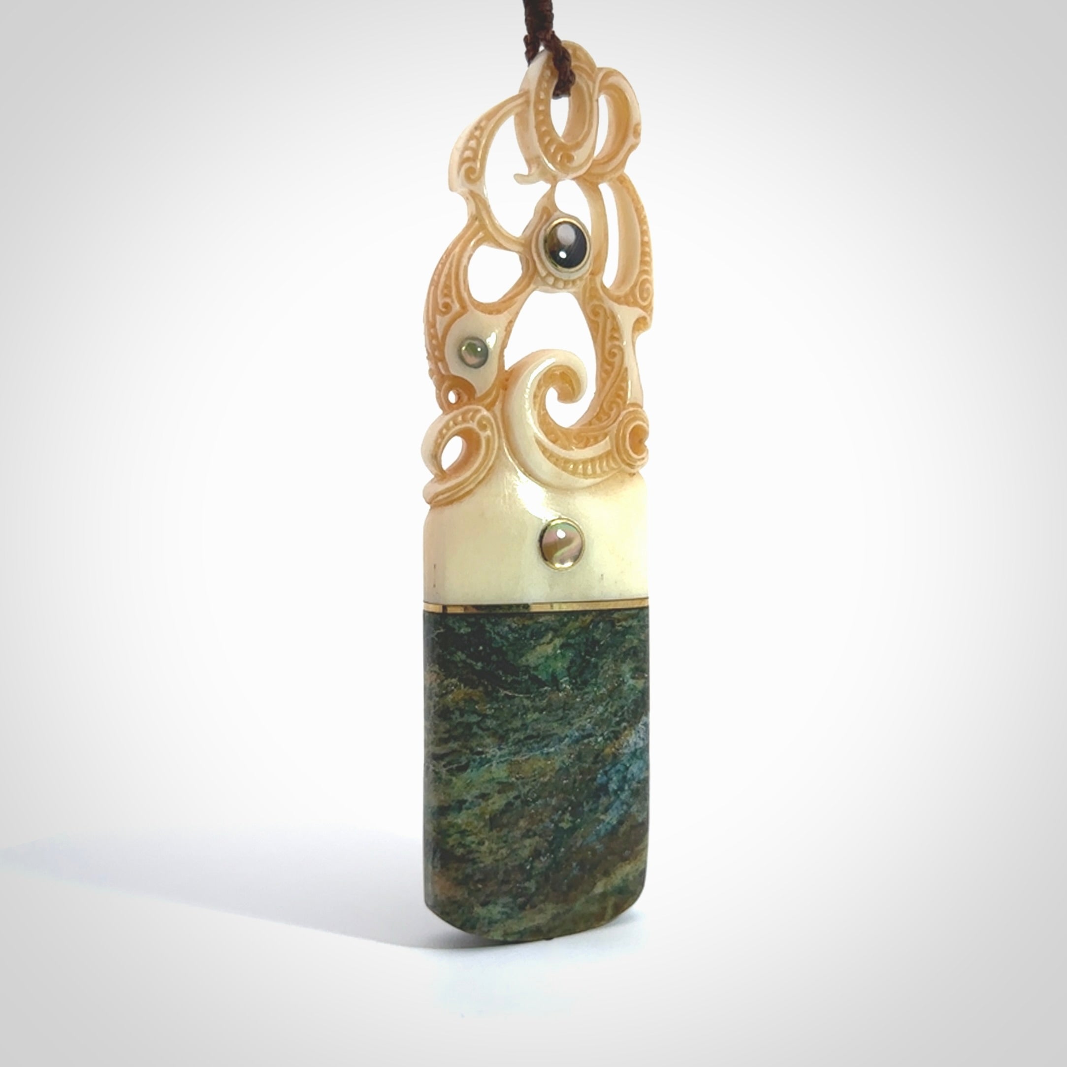 This is a large carved Manaia pendant. It is made from unique materials - New Zealand Obay Stone, Bone, Paua shell, Brass and Mother of Pearl. The face of the Manaia is carved with a traditional design in the front. It is carved front and back and has traditional carved designs. This is a large and very traditional pendant that is a collectors piece.