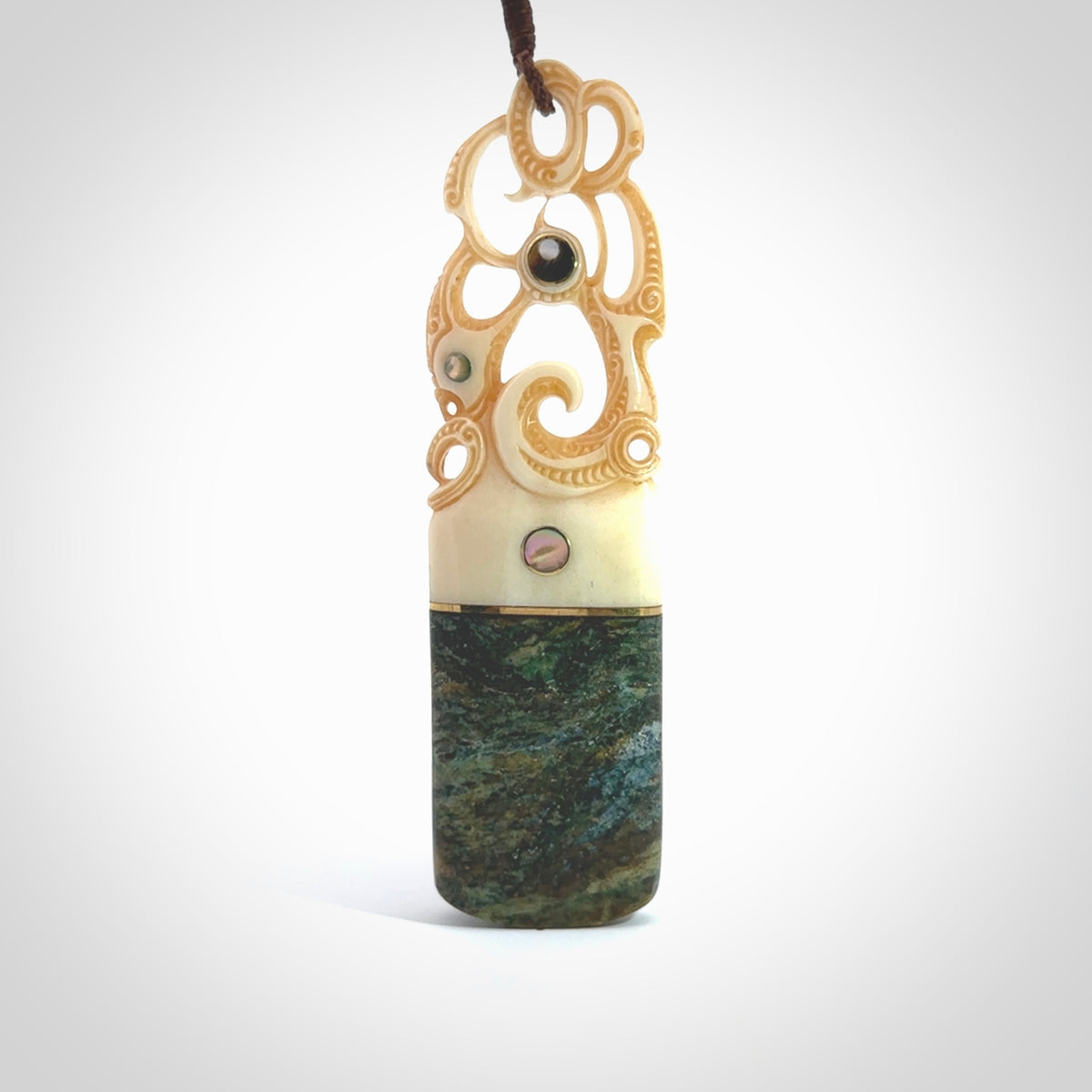 This is a large carved Manaia pendant. It is made from unique materials - New Zealand Obay Stone, Bone, Paua shell, Brass and Mother of Pearl. The face of the Manaia is carved with a traditional design in the front. It is carved front and back and has traditional carved designs. This is a large and very traditional pendant that is a collectors piece.