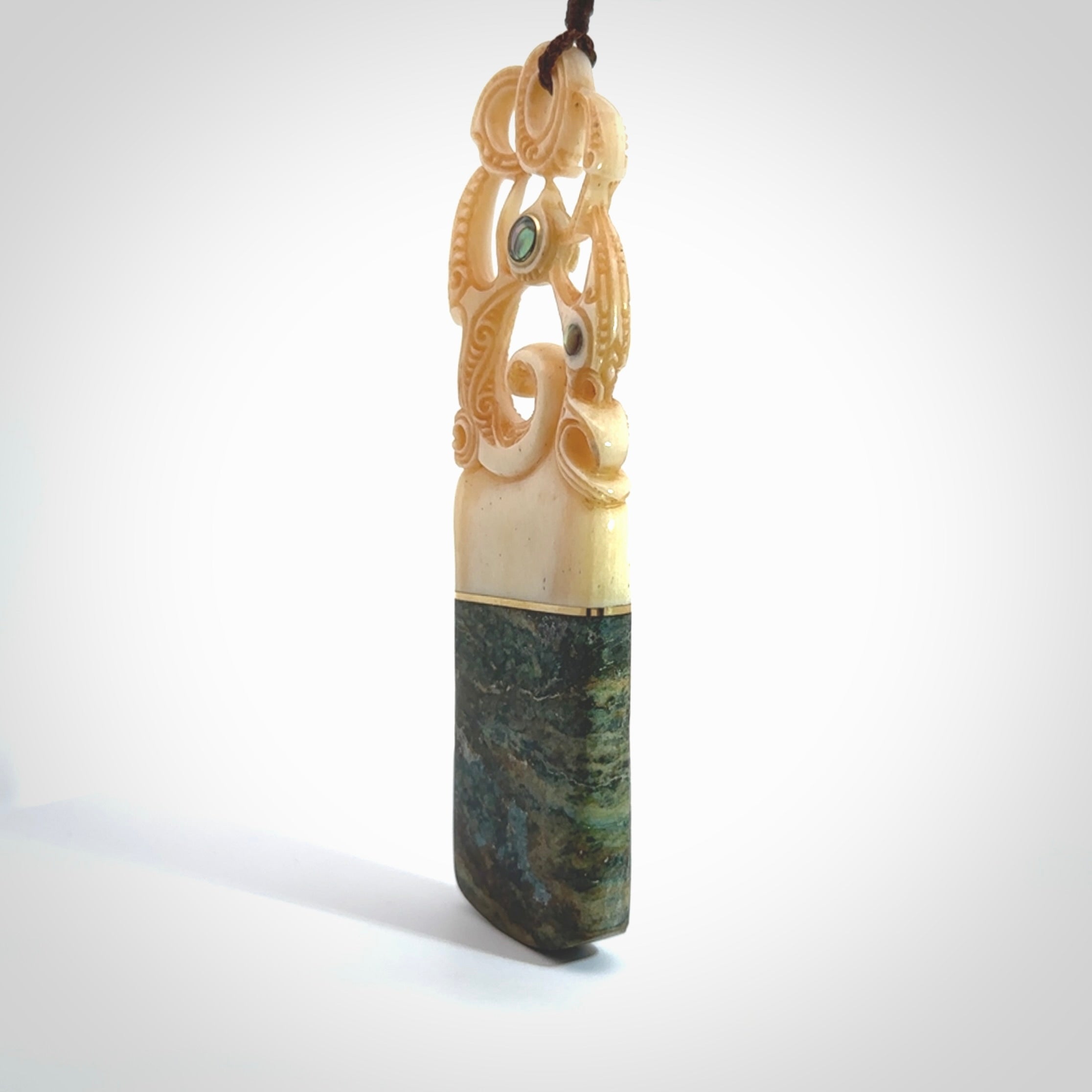 This is a large carved Manaia pendant. It is made from unique materials - New Zealand Obay Stone, Bone, Paua shell, Brass and Mother of Pearl. The face of the Manaia is carved with a traditional design in the front. It is carved front and back and has traditional carved designs. This is a large and very traditional pendant that is a collectors piece.