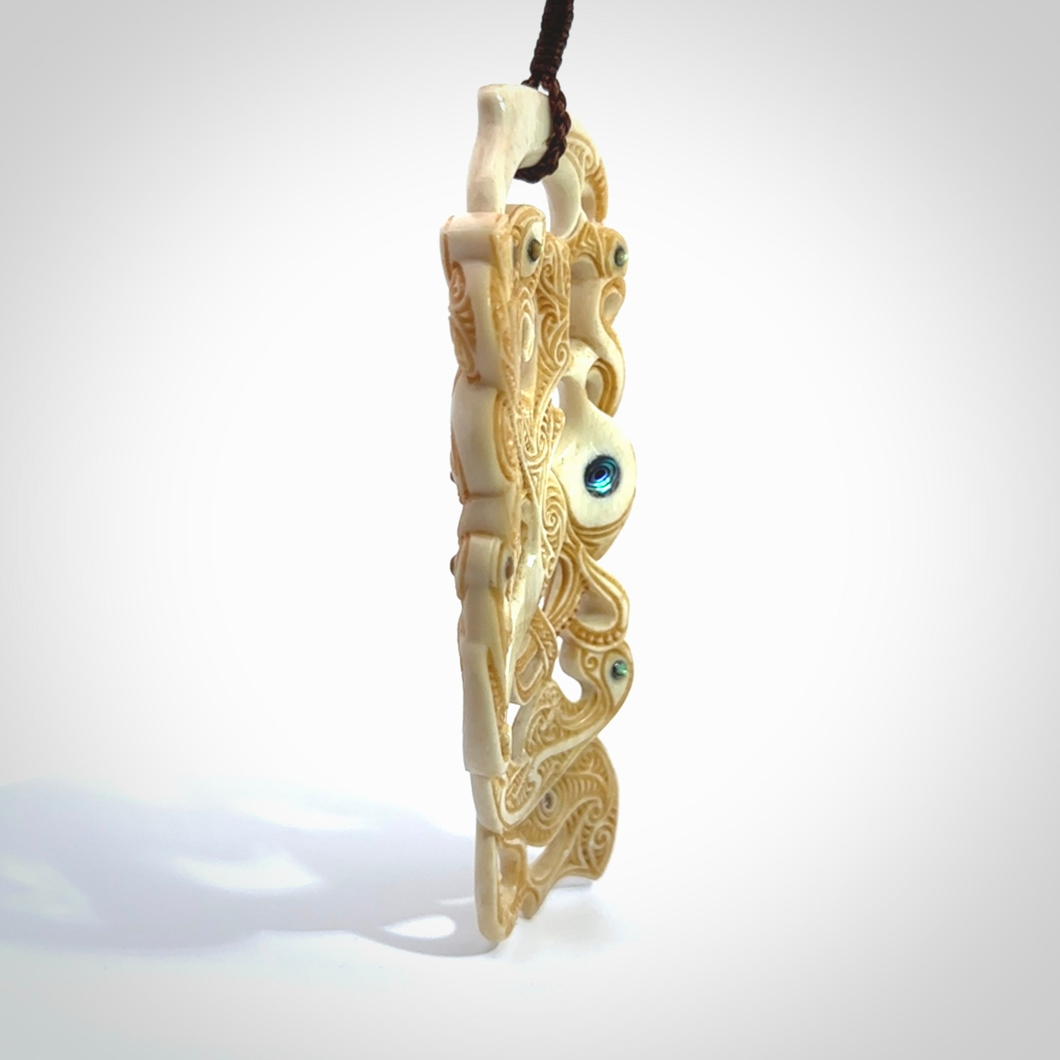 This picture shows a carved Tiki and manaia in bone. The artist, Andrew Doughty, has carved traditional decorative Koru designs into the face of the body and these run up the sides of the manaia head. These have specific meanings. It is provided with a hand-plaited brown cord that is length adjustable.