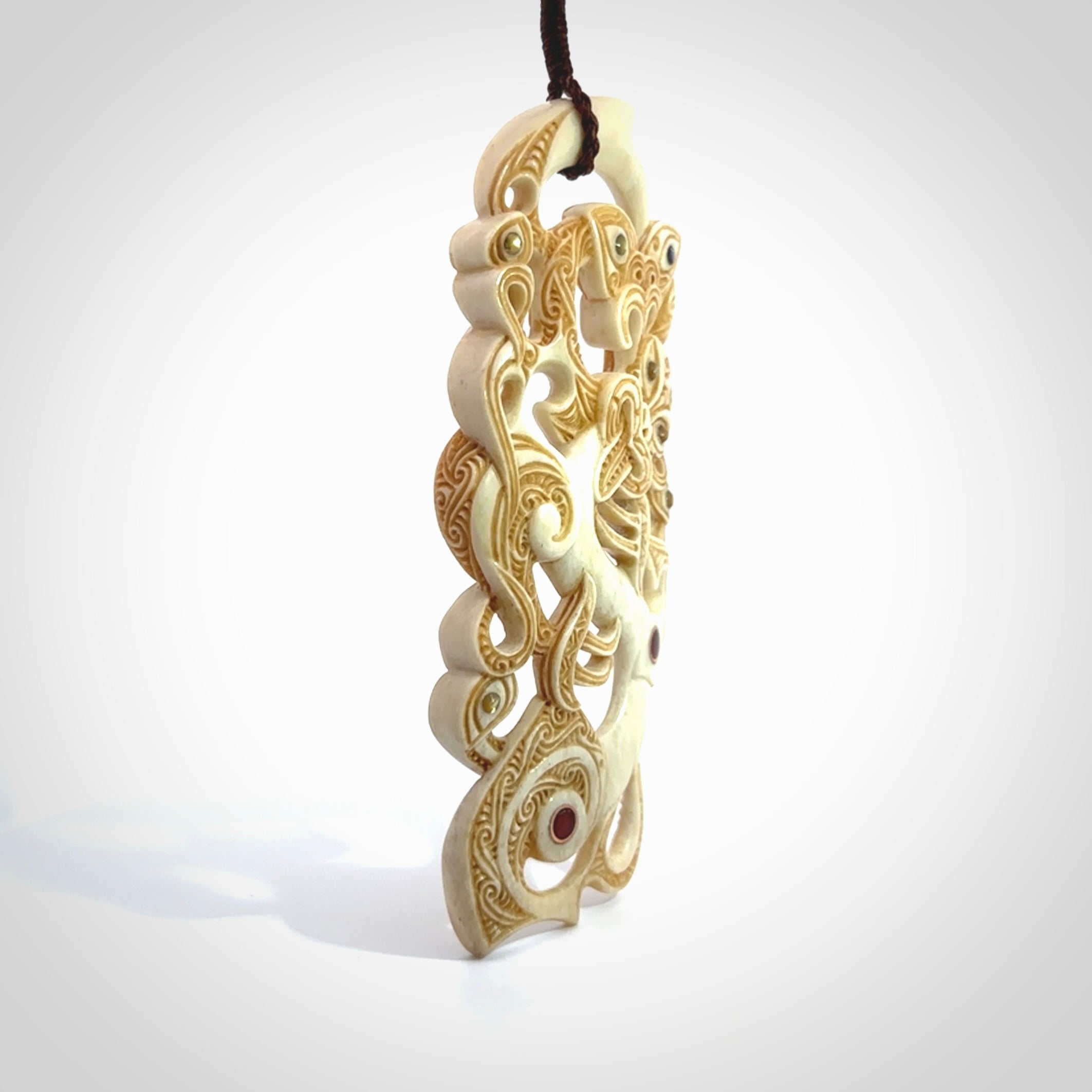 This picture shows a carved Tiki and manaia in bone. The artist, Andrew Doughty, has carved traditional decorative Koru designs into the face of the body and these run up the sides of the manaia head. These have specific meanings. It is provided with a hand-plaited brown cord that is length adjustable.