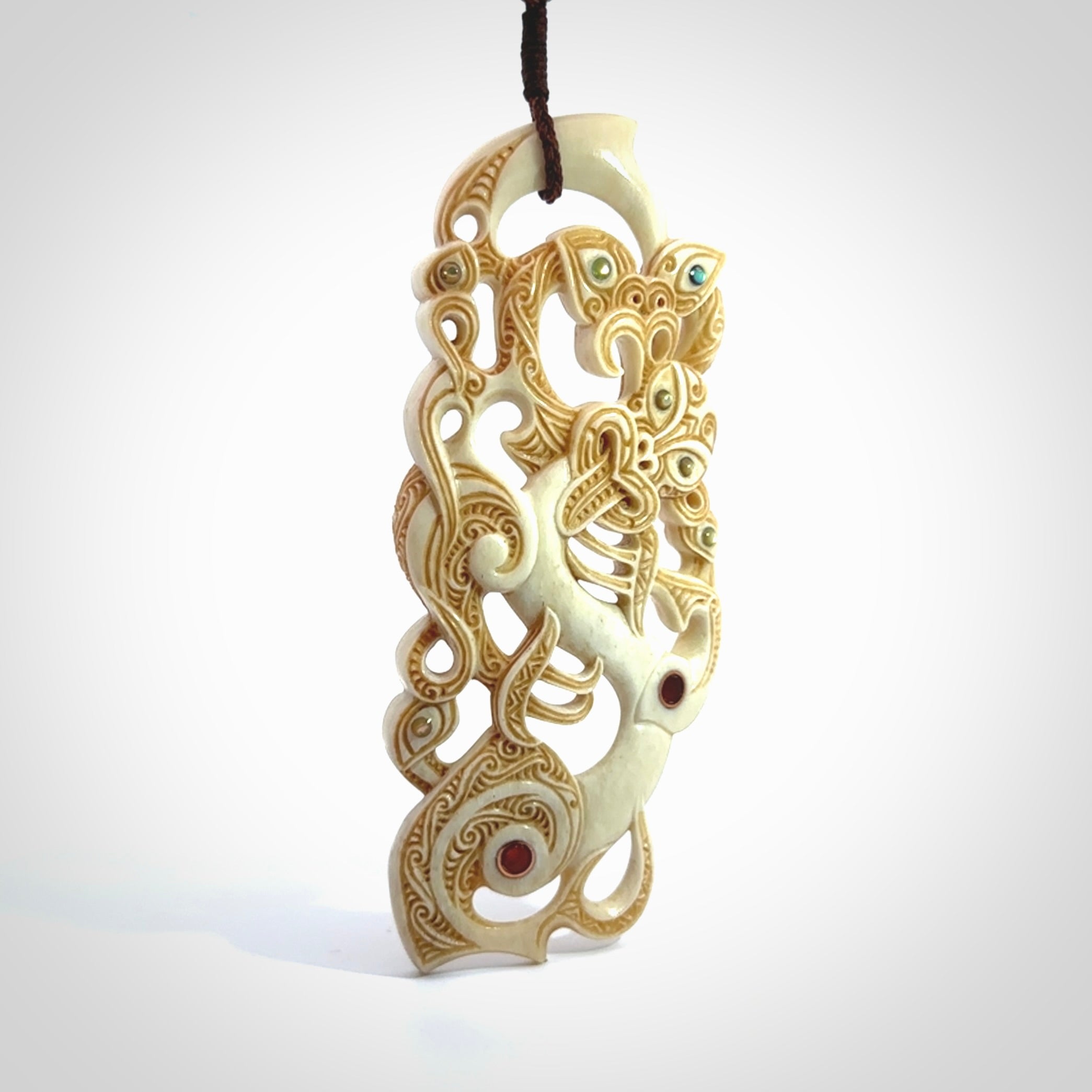 This picture shows a carved Tiki and manaia in bone. The artist, Andrew Doughty, has carved traditional decorative Koru designs into the face of the body and these run up the sides of the manaia head. These have specific meanings. It is provided with a hand-plaited brown cord that is length adjustable.