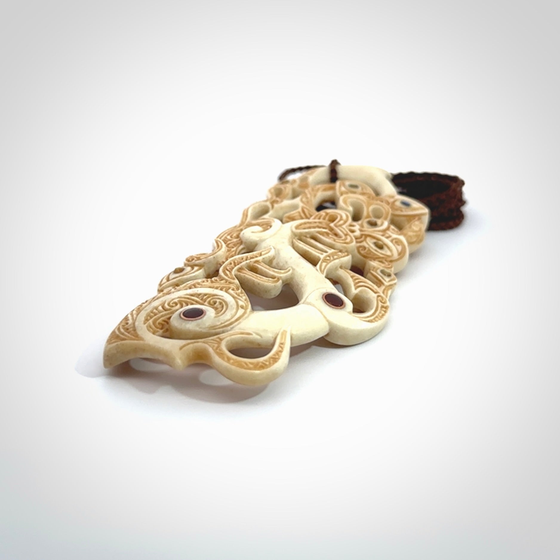 This picture shows a carved Tiki and manaia in bone. The artist, Andrew Doughty, has carved traditional decorative Koru designs into the face of the body and these run up the sides of the manaia head. These have specific meanings. It is provided with a hand-plaited brown cord that is length adjustable.