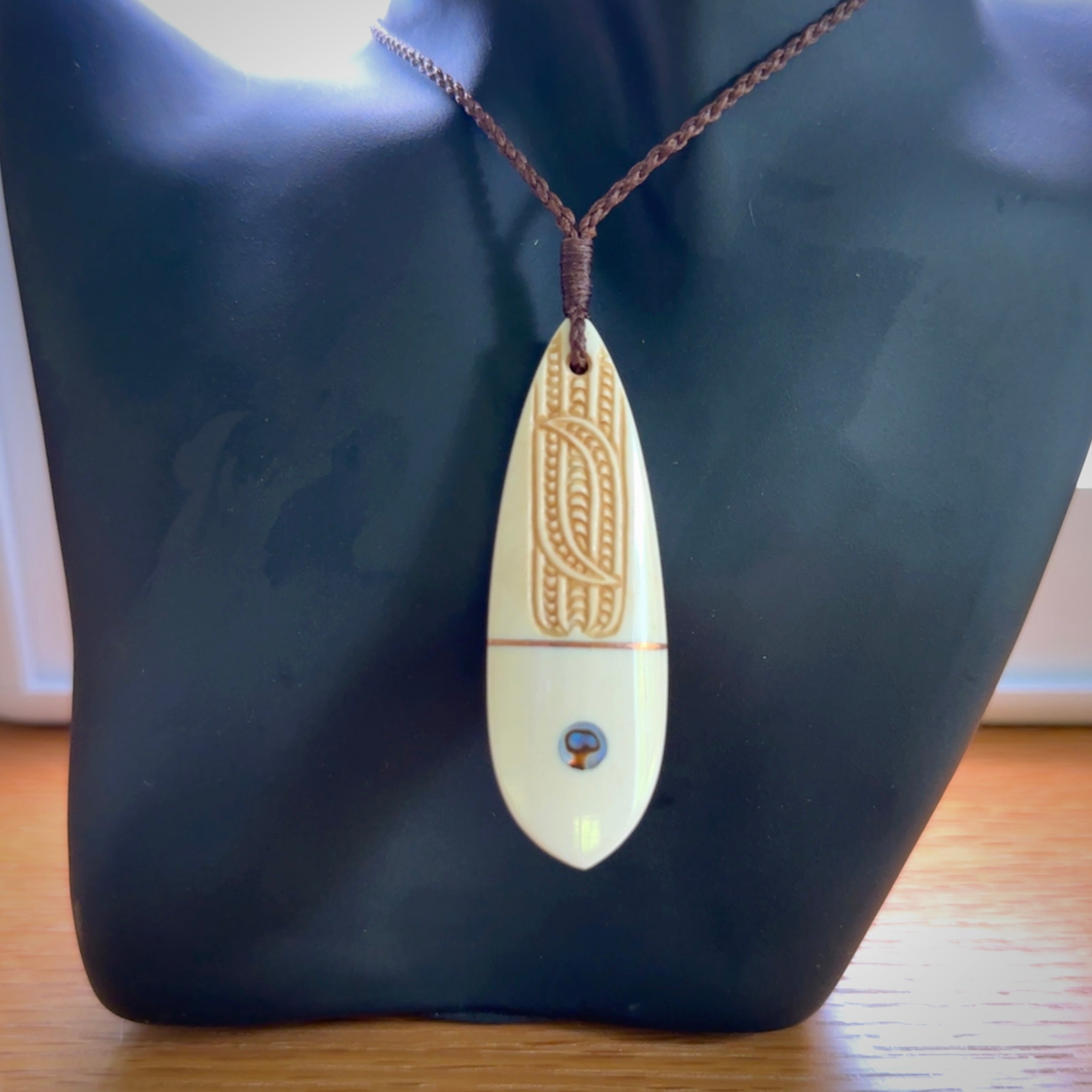 This is a wonderful, finely carved drop pendant. It is hand carved by Andrew Doughty and we will ship it to you free anywhere in the world. Hand made from bone with Paua shell and copper inlay. Delivered with an adjustable brown cord.