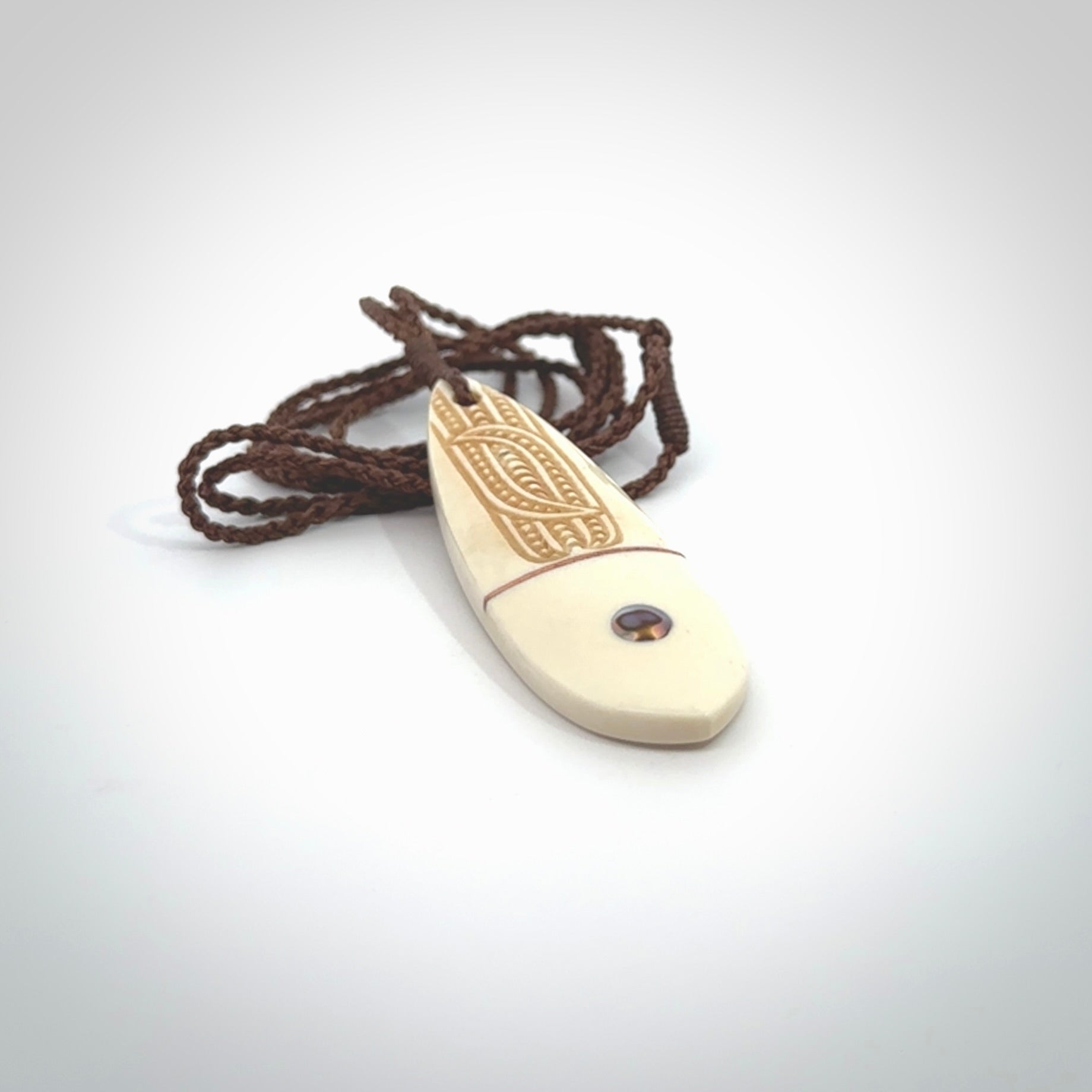 This is a wonderful, finely carved drop pendant. It is hand carved by Andrew Doughty and we will ship it to you free anywhere in the world. Hand made from bone with Paua shell and copper inlay. Delivered with an adjustable brown cord.