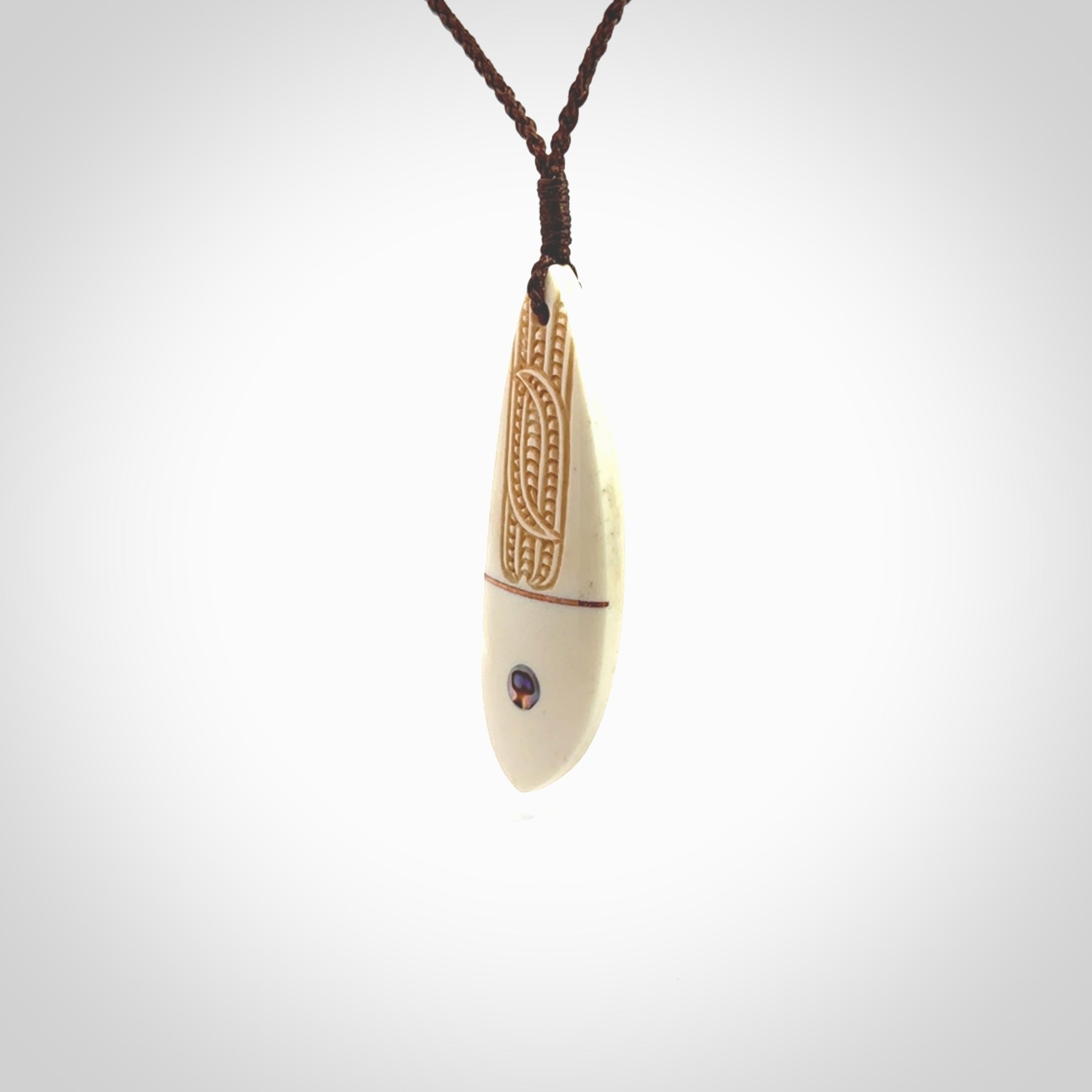 This is a wonderful, finely carved drop pendant. It is hand carved by Andrew Doughty and we will ship it to you free anywhere in the world. Hand made from bone with Paua shell and copper inlay. Delivered with an adjustable brown cord.