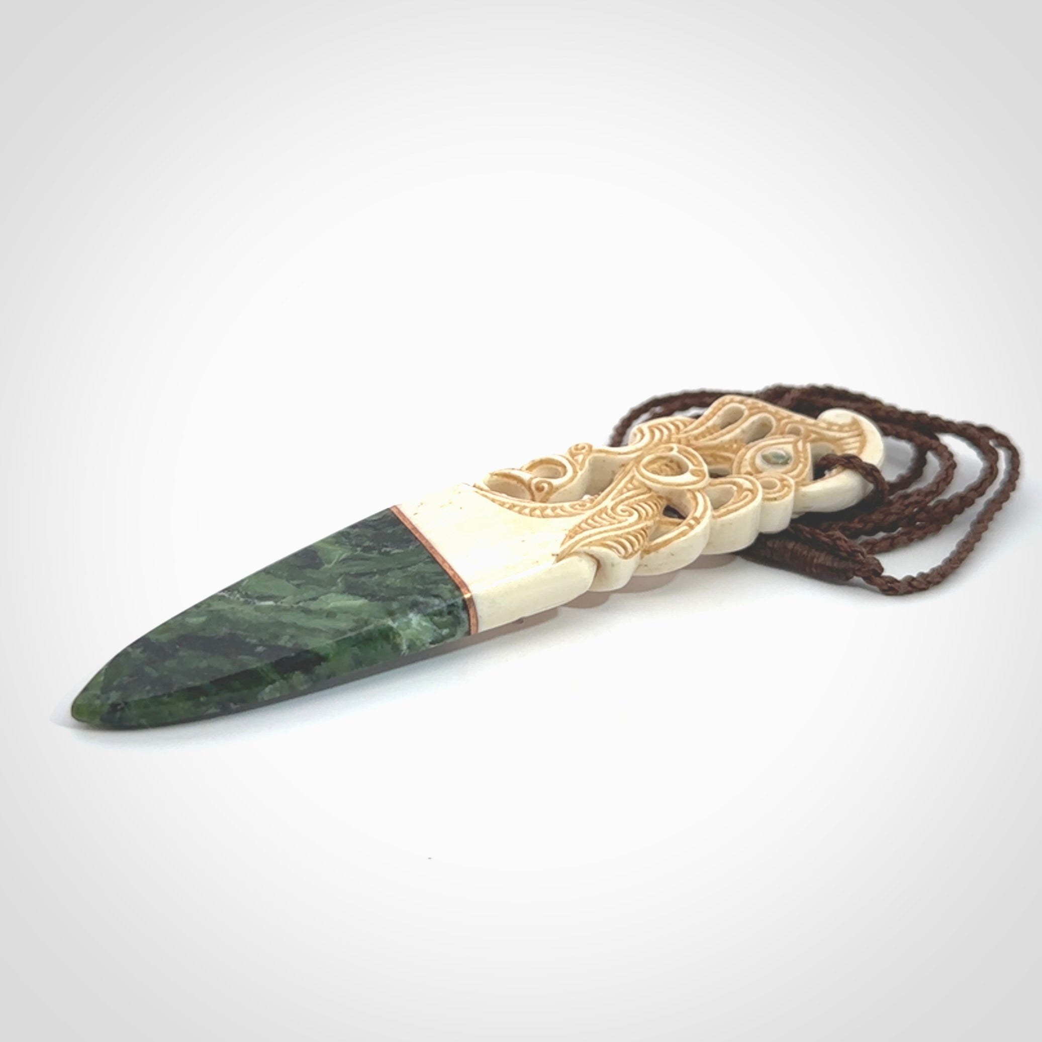 This is a large carved Manaia pendant. It is made from three materials - New Zealand Jade, Bone, Paua shell, Copper. The face of the Manaia is carved with a traditional design in the front. It has a protruding tongue which is also carved and the back face has traditional carved designs. This is a large and very traditional pendant that is a collectors piece.