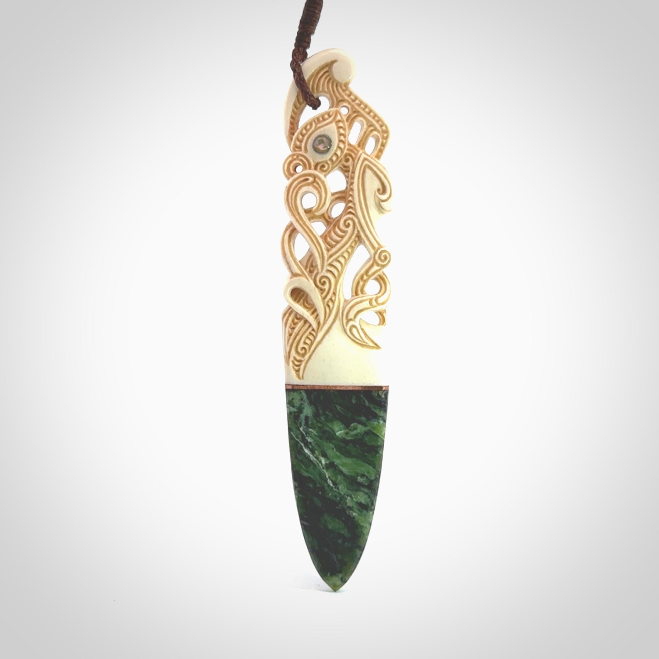 This is a large carved Manaia pendant. It is made from three materials - New Zealand Jade, Bone, Paua shell, Copper. The face of the Manaia is carved with a traditional design in the front. It has a protruding tongue which is also carved and the back face has traditional carved designs. This is a large and very traditional pendant that is a collectors piece.