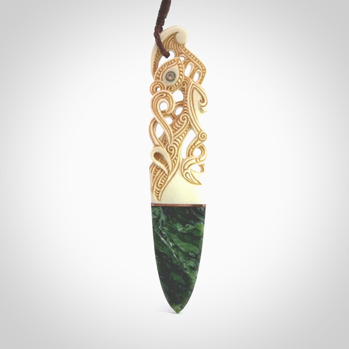 This is a large carved Manaia pendant. It is made from three materials - New Zealand Jade, Bone, Paua shell, Copper. The face of the Manaia is carved with a traditional design in the front. It has a protruding tongue which is also carved and the back face has traditional carved designs. This is a large and very traditional pendant that is a collectors piece.