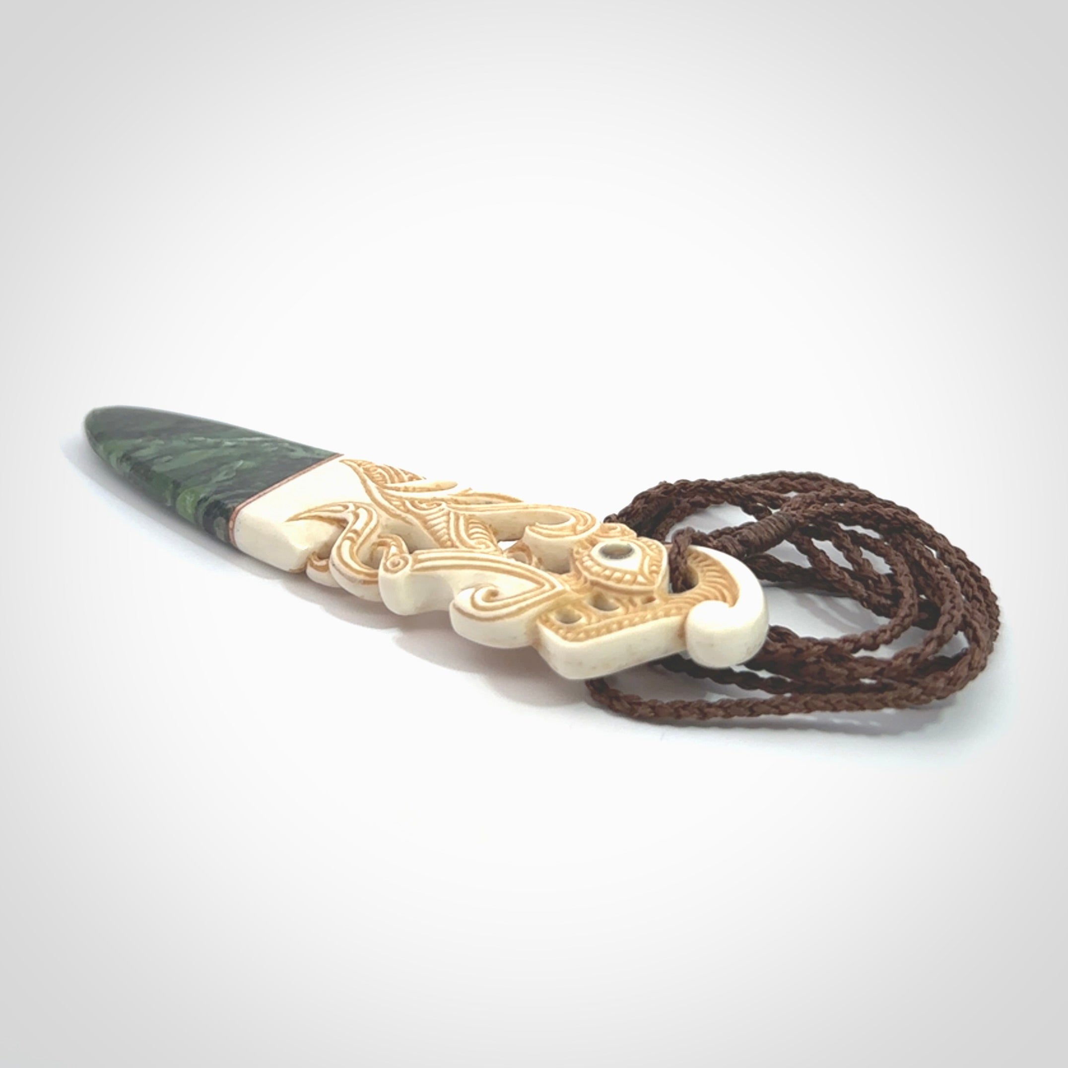 This is a large carved Manaia pendant. It is made from three materials - New Zealand Jade, Bone, Paua shell, Copper. The face of the Manaia is carved with a traditional design in the front. It has a protruding tongue which is also carved and the back face has traditional carved designs. This is a large and very traditional pendant that is a collectors piece.