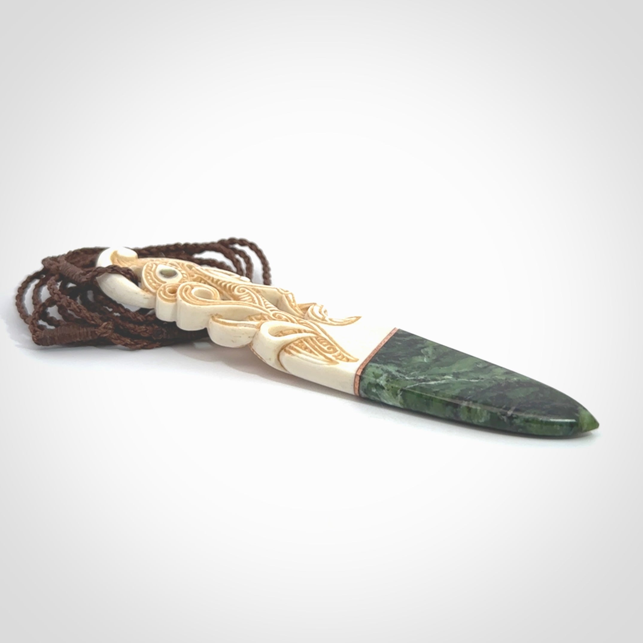 This is a large carved Manaia pendant. It is made from three materials - New Zealand Jade, Bone, Paua shell, Copper. The face of the Manaia is carved with a traditional design in the front. It has a protruding tongue which is also carved and the back face has traditional carved designs. This is a large and very traditional pendant that is a collectors piece.