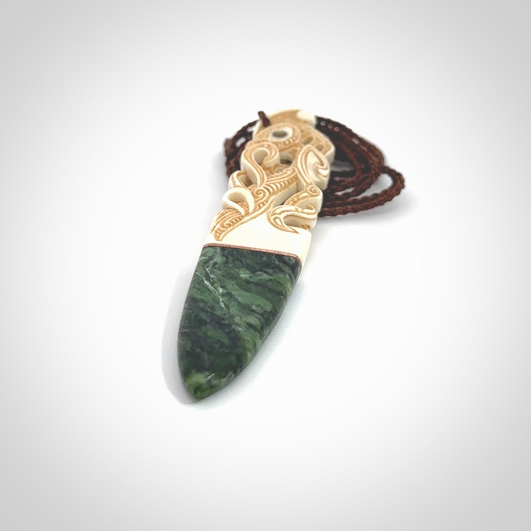 This is a large carved Manaia pendant. It is made from three materials - New Zealand Jade, Bone, Paua shell, Copper. The face of the Manaia is carved with a traditional design in the front. It has a protruding tongue which is also carved and the back face has traditional carved designs. This is a large and very traditional pendant that is a collectors piece.