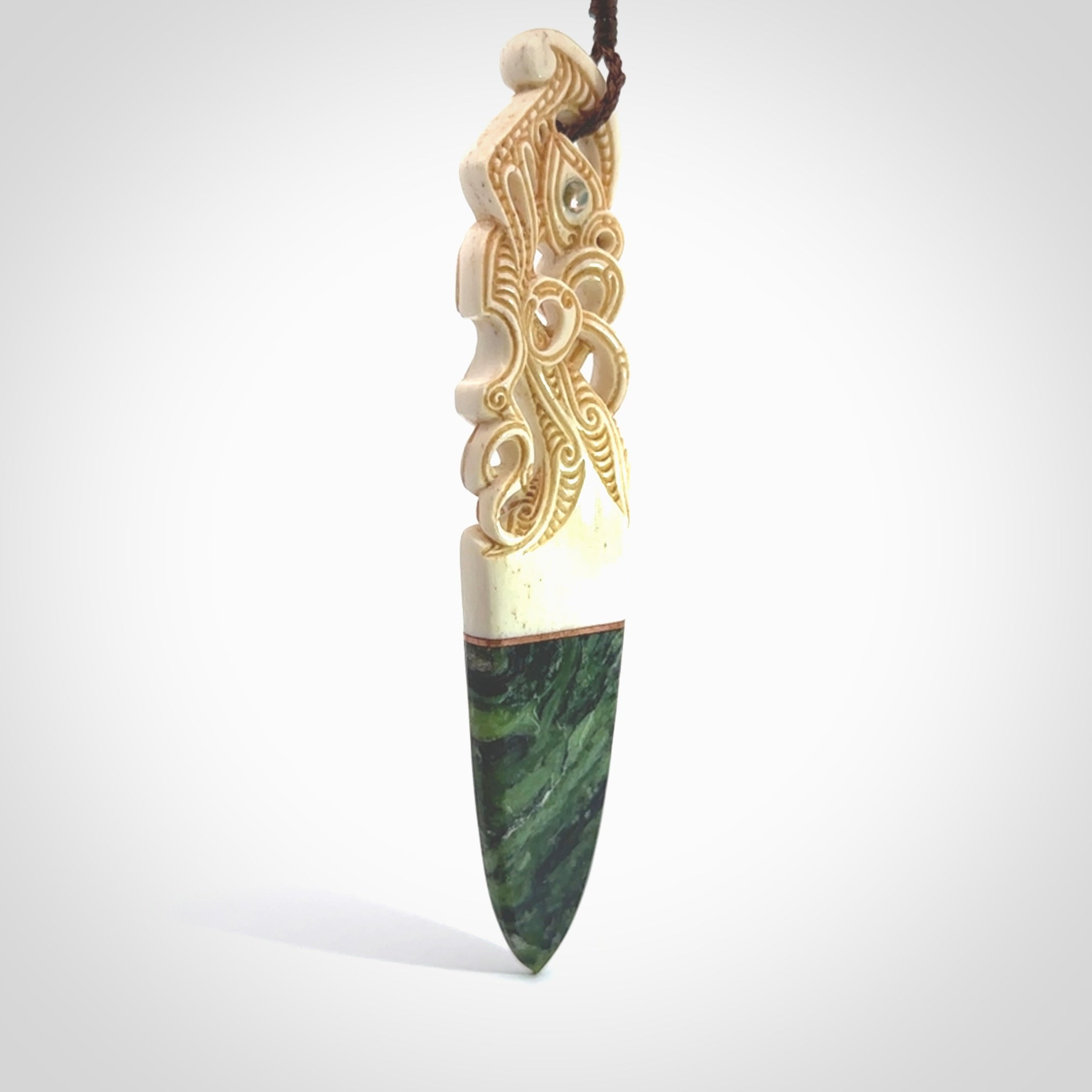 This is a large carved Manaia pendant. It is made from three materials - New Zealand Jade, Bone, Paua shell, Copper. The face of the Manaia is carved with a traditional design in the front. It has a protruding tongue which is also carved and the back face has traditional carved designs. This is a large and very traditional pendant that is a collectors piece.