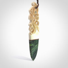 This is a large carved Manaia pendant. It is made from three materials - New Zealand Jade, Bone, Paua shell, Copper. The face of the Manaia is carved with a traditional design in the front. It has a protruding tongue which is also carved and the back face has traditional carved designs. This is a large and very traditional pendant that is a collectors piece.