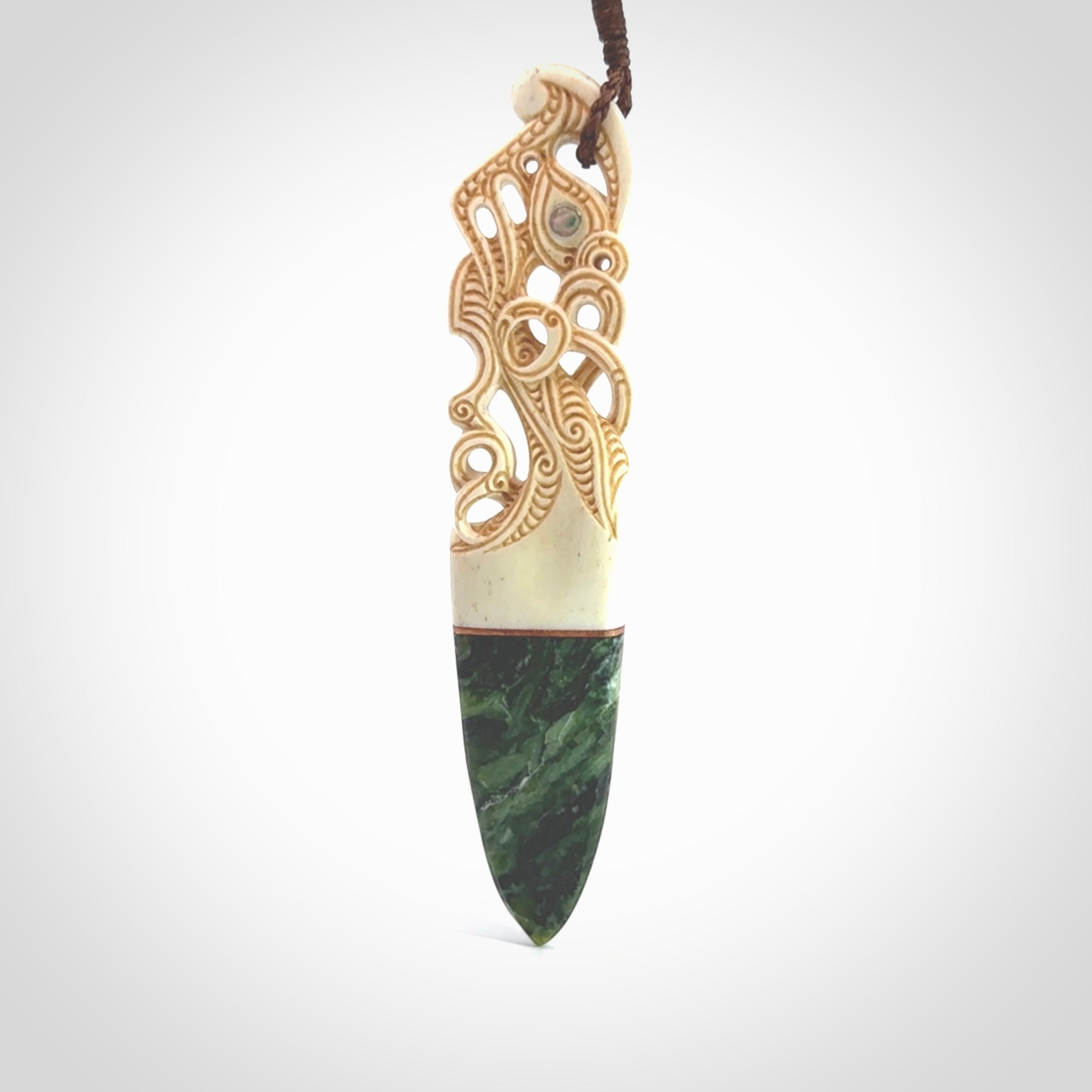 This is a large carved Manaia pendant. It is made from three materials - New Zealand Jade, Bone, Paua shell, Copper. The face of the Manaia is carved with a traditional design in the front. It has a protruding tongue which is also carved and the back face has traditional carved designs. This is a large and very traditional pendant that is a collectors piece.