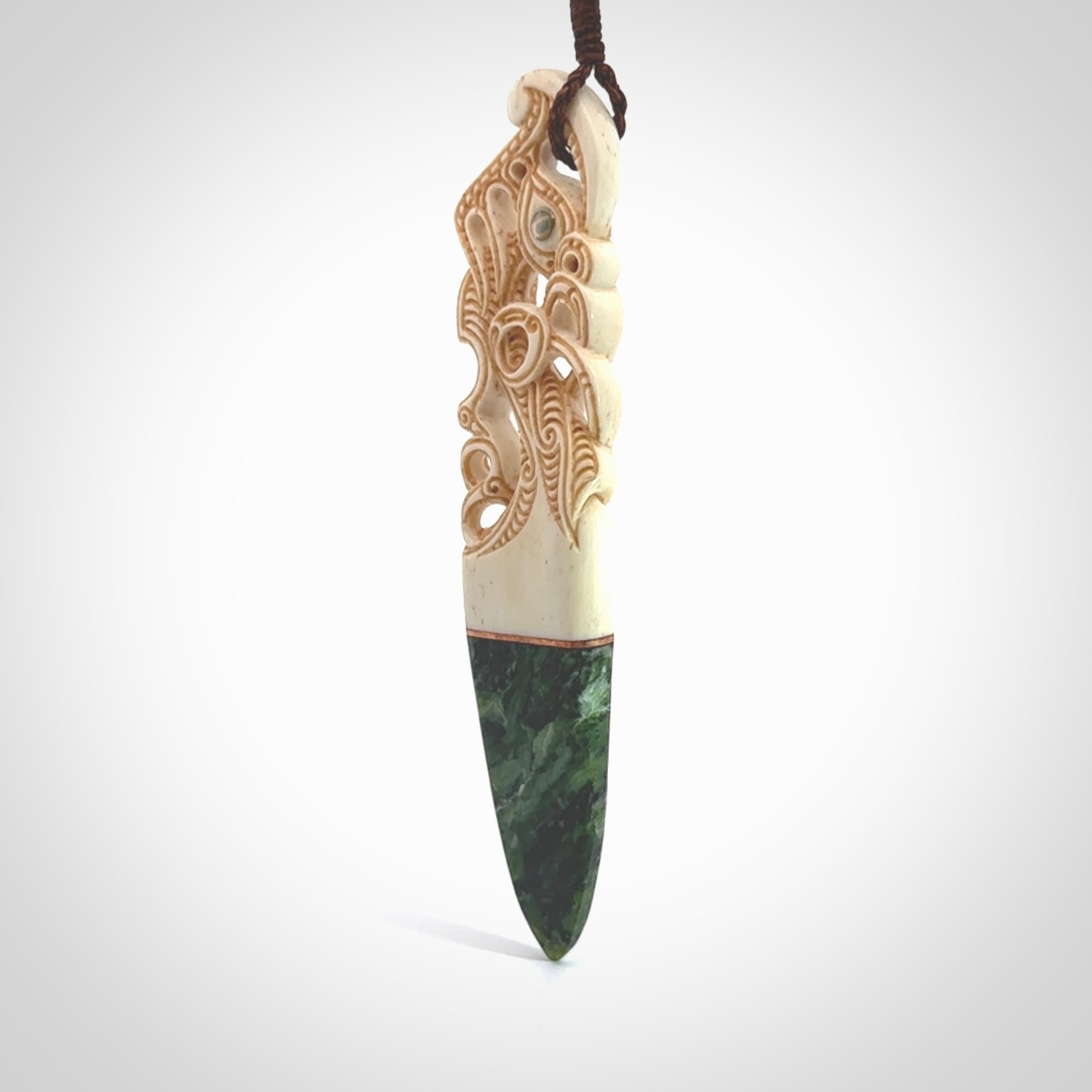 This is a large carved Manaia pendant. It is made from three materials - New Zealand Jade, Bone, Paua shell, Copper. The face of the Manaia is carved with a traditional design in the front. It has a protruding tongue which is also carved and the back face has traditional carved designs. This is a large and very traditional pendant that is a collectors piece.