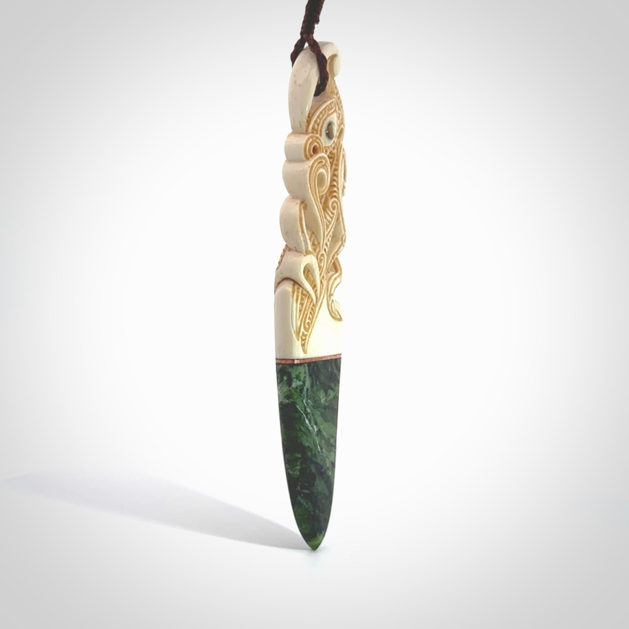 This is a large carved Manaia pendant. It is made from three materials - New Zealand Jade, Bone, Paua shell, Copper. The face of the Manaia is carved with a traditional design in the front. It has a protruding tongue which is also carved and the back face has traditional carved designs. This is a large and very traditional pendant that is a collectors piece.