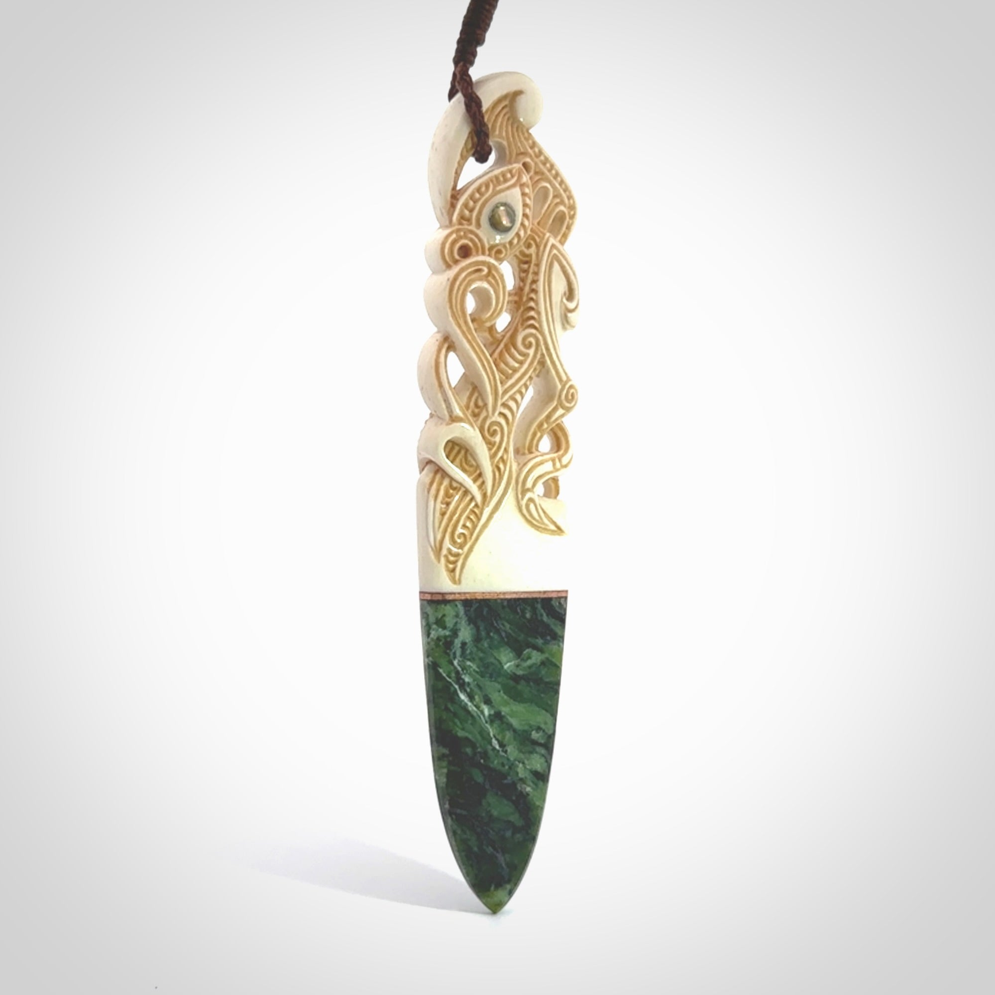 This is a large carved Manaia pendant. It is made from three materials - New Zealand Jade, Bone, Paua shell, Copper. The face of the Manaia is carved with a traditional design in the front. It has a protruding tongue which is also carved and the back face has traditional carved designs. This is a large and very traditional pendant that is a collectors piece.