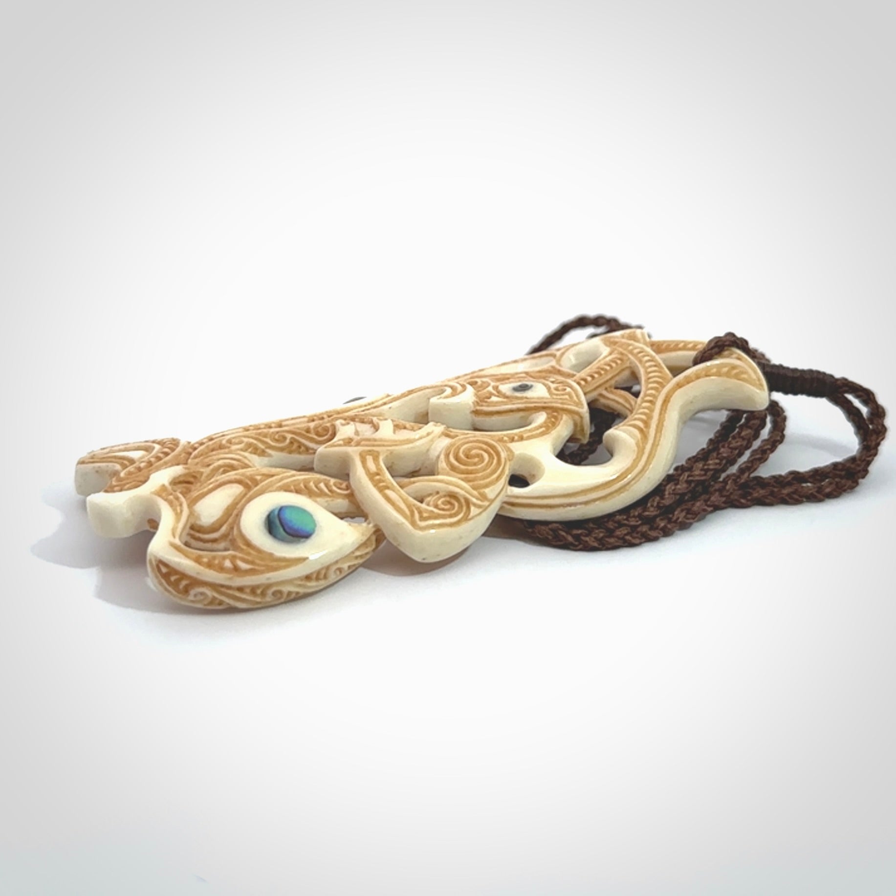 This is a wonderful, finely carved Manaia with Tiki drop pendant. It is hand carved by Andrew Doughty and we will ship it to you free anywhere in the world. Hand made from bone and delivered to you with an adjustable brown cord.