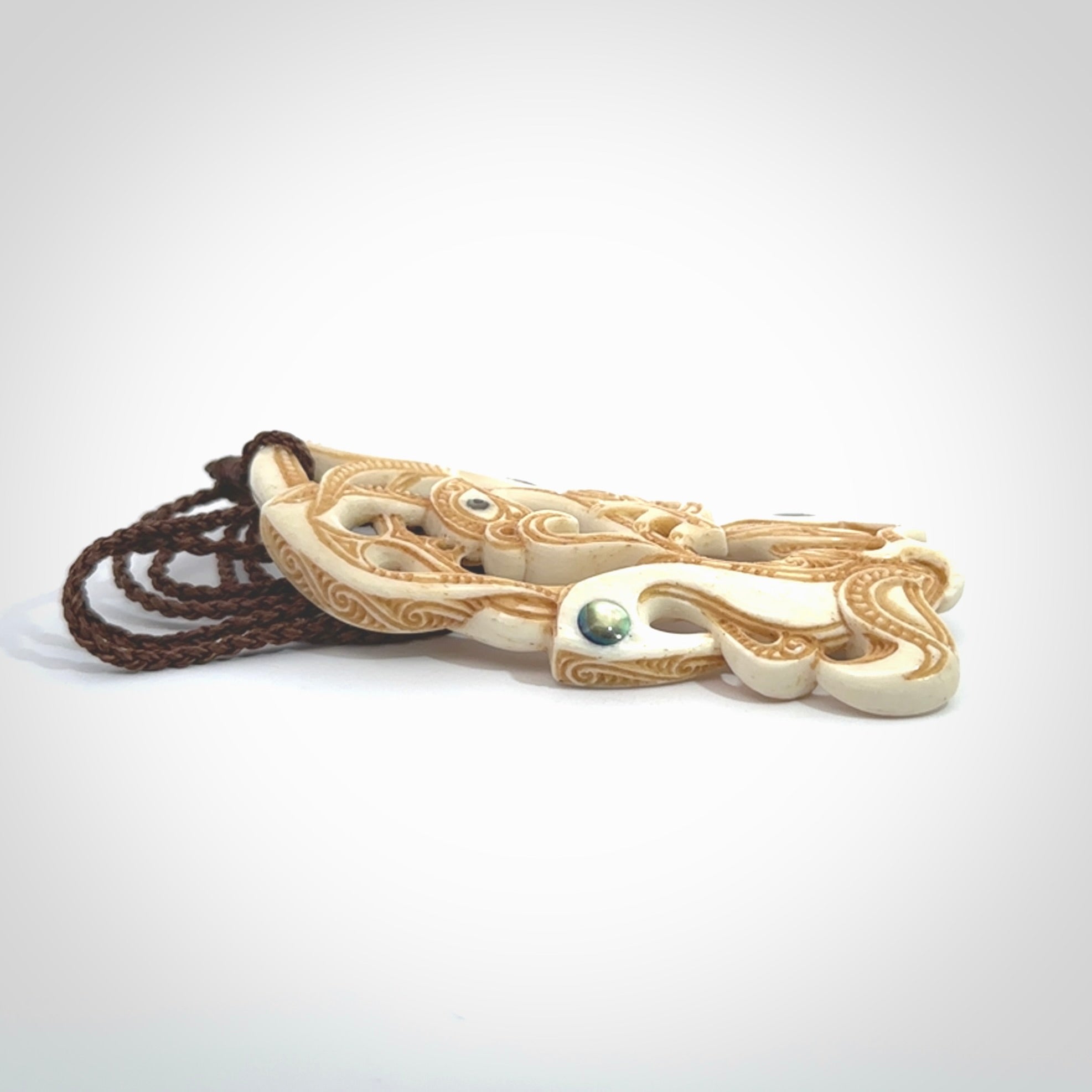 This is a wonderful, finely carved Manaia with Tiki drop pendant. It is hand carved by Andrew Doughty and we will ship it to you free anywhere in the world. Hand made from bone and delivered to you with an adjustable brown cord.