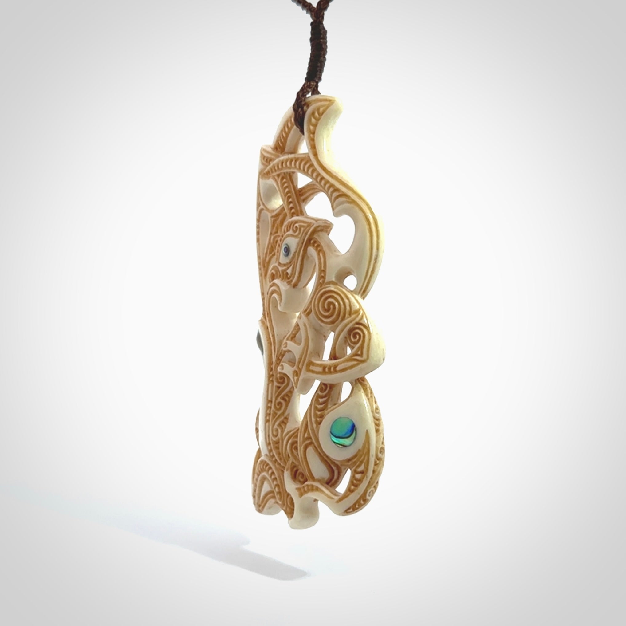 This is a wonderful, finely carved Manaia with Tiki drop pendant. It is hand carved by Andrew Doughty and we will ship it to you free anywhere in the world. Hand made from bone and delivered to you with an adjustable brown cord.