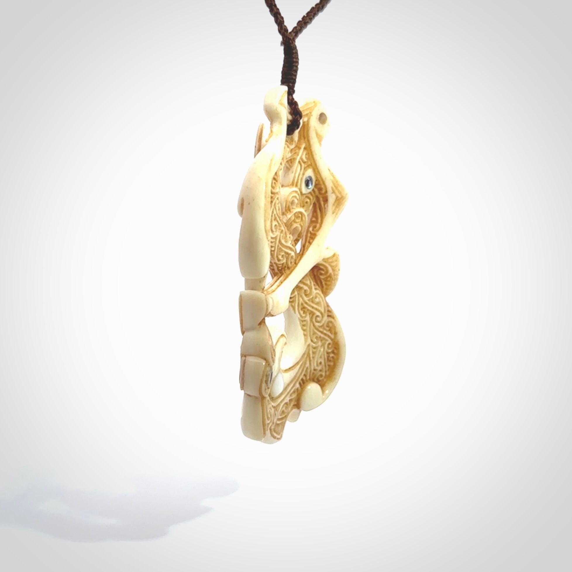 This is a wonderful, finely carved Manaia with Tiki drop pendant. It is hand carved by Andrew Doughty and we will ship it to you free anywhere in the world. Hand made from bone and delivered to you with an adjustable brown cord.