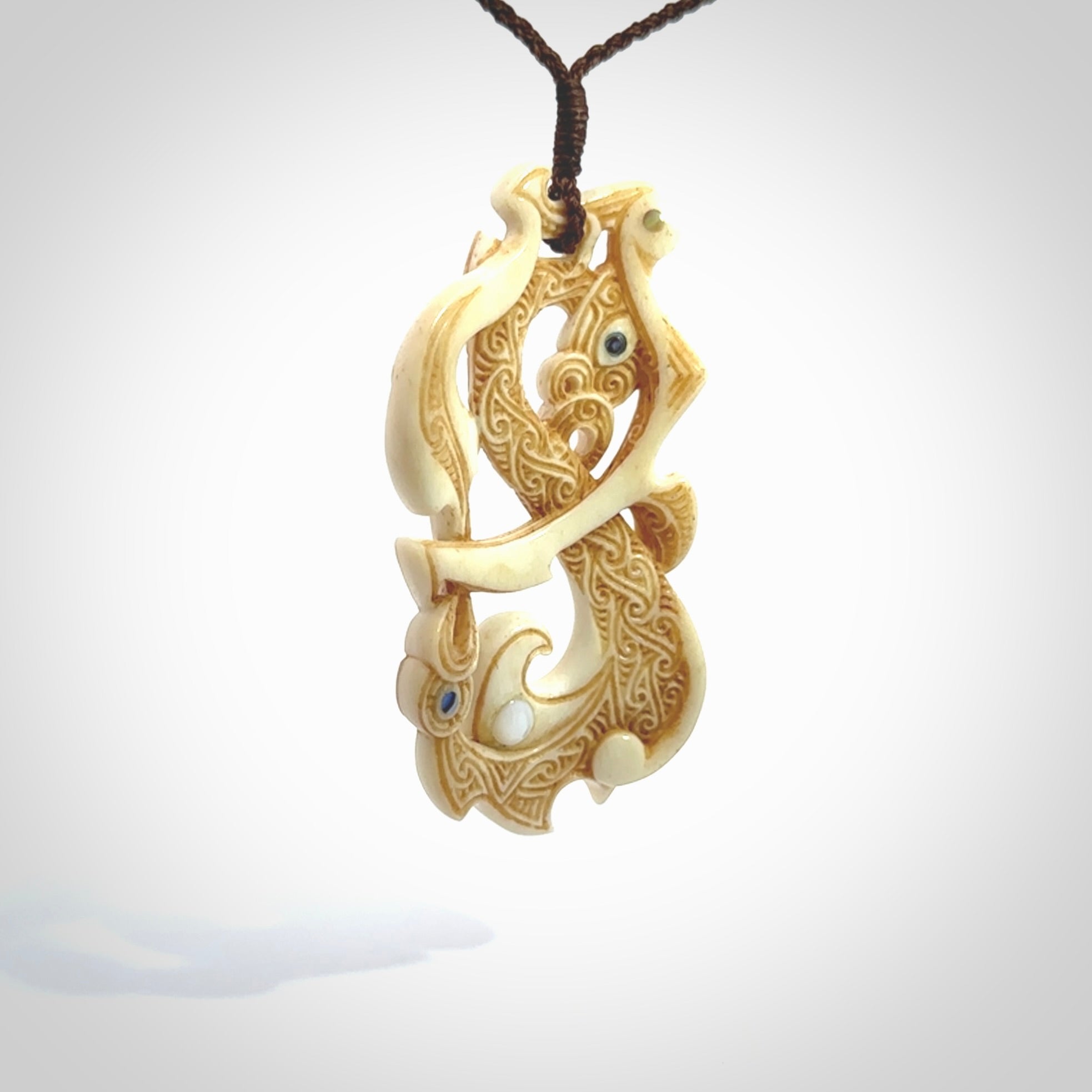 This is a wonderful, finely carved Manaia with Tiki drop pendant. It is hand carved by Andrew Doughty and we will ship it to you free anywhere in the world. Hand made from bone and delivered to you with an adjustable brown cord.