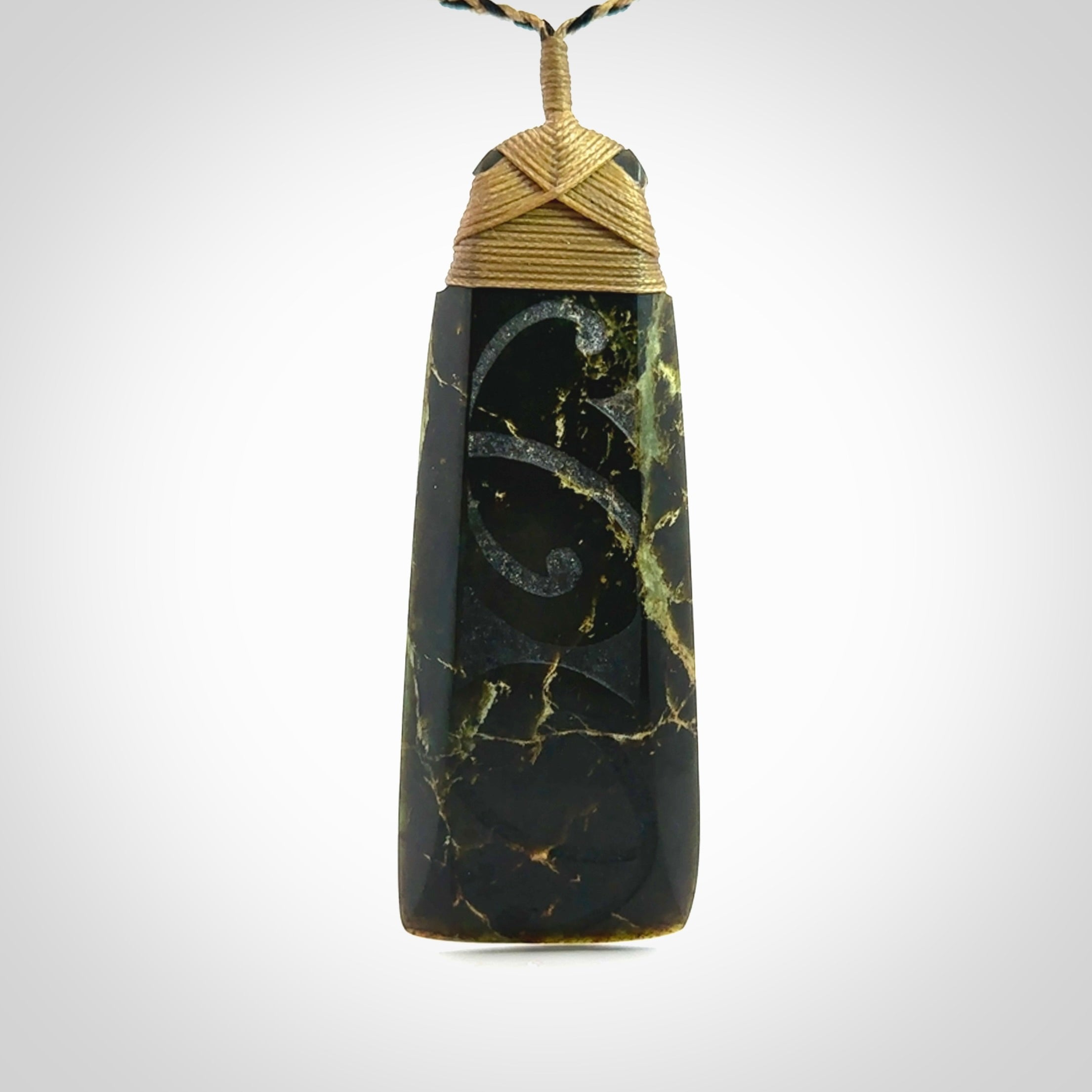 Large Jade Toki pendant. Hand carved from a lovely piece of local New Zealand Jade. The quality of the workmanship and design is outstanding - this is a piece you will want to wear all the time. We have suspended this from an adjustable 3-plait tan/black cord and tan binding.