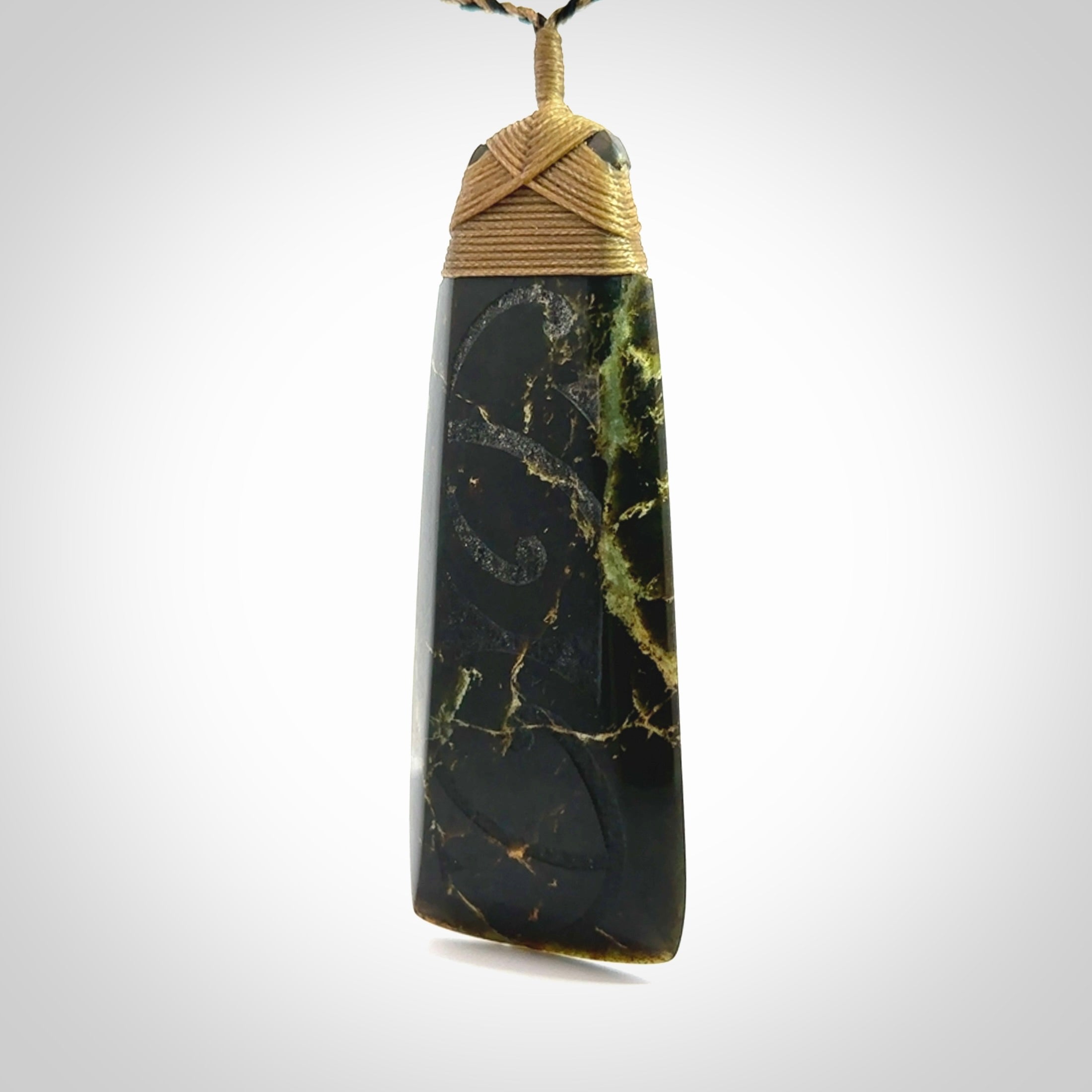 Large Jade Toki pendant. Hand carved from a lovely piece of local New Zealand Jade. The quality of the workmanship and design is outstanding - this is a piece you will want to wear all the time. We have suspended this from an adjustable 3-plait tan/black cord and tan binding.