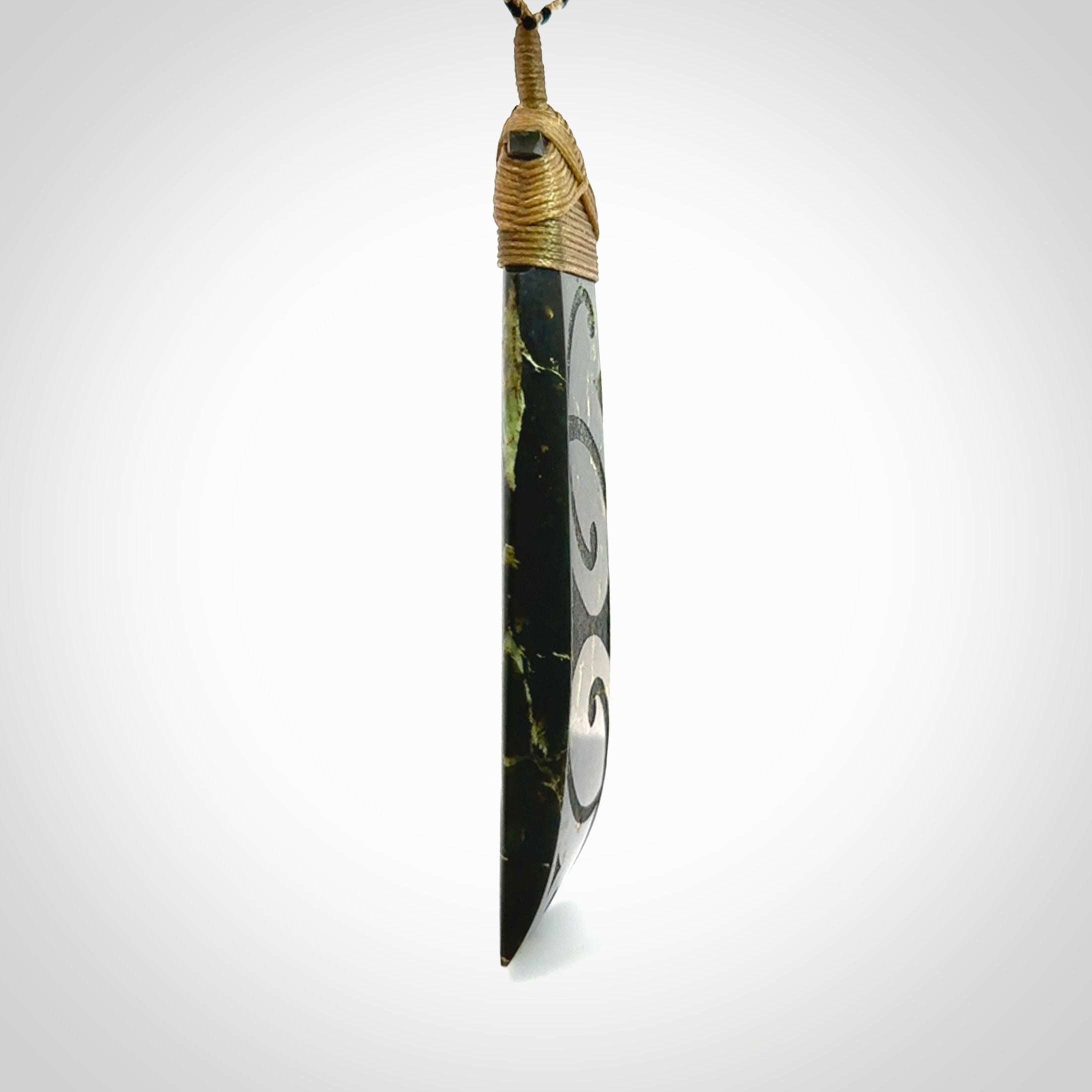 Large Jade Toki pendant. Hand carved from a lovely piece of local New Zealand Jade. The quality of the workmanship and design is outstanding - this is a piece you will want to wear all the time. We have suspended this from an adjustable 3-plait tan/black cord and tan binding.