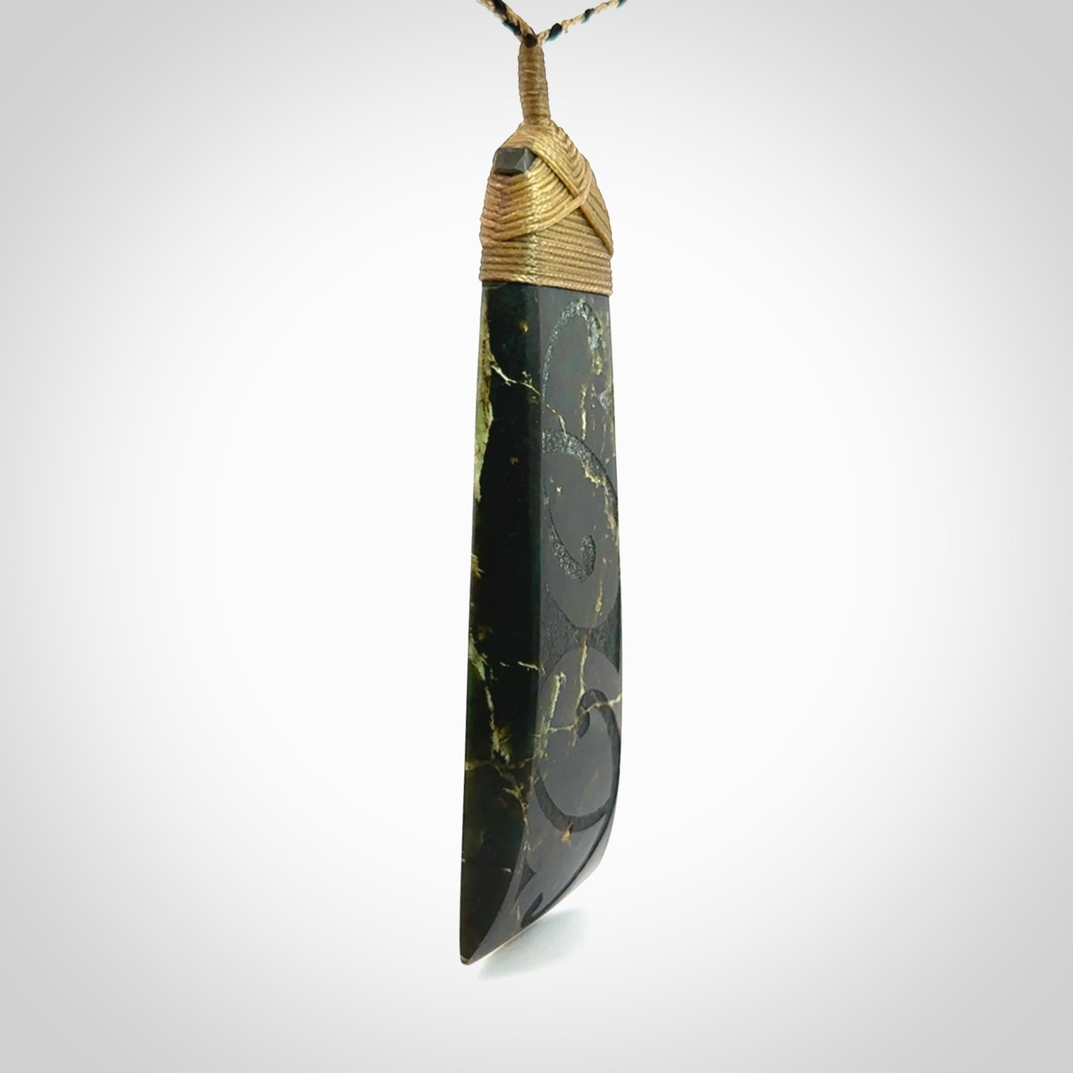 Large Jade Toki pendant. Hand carved from a lovely piece of local New Zealand Jade. The quality of the workmanship and design is outstanding - this is a piece you will want to wear all the time. We have suspended this from an adjustable 3-plait tan/black cord and tan binding.