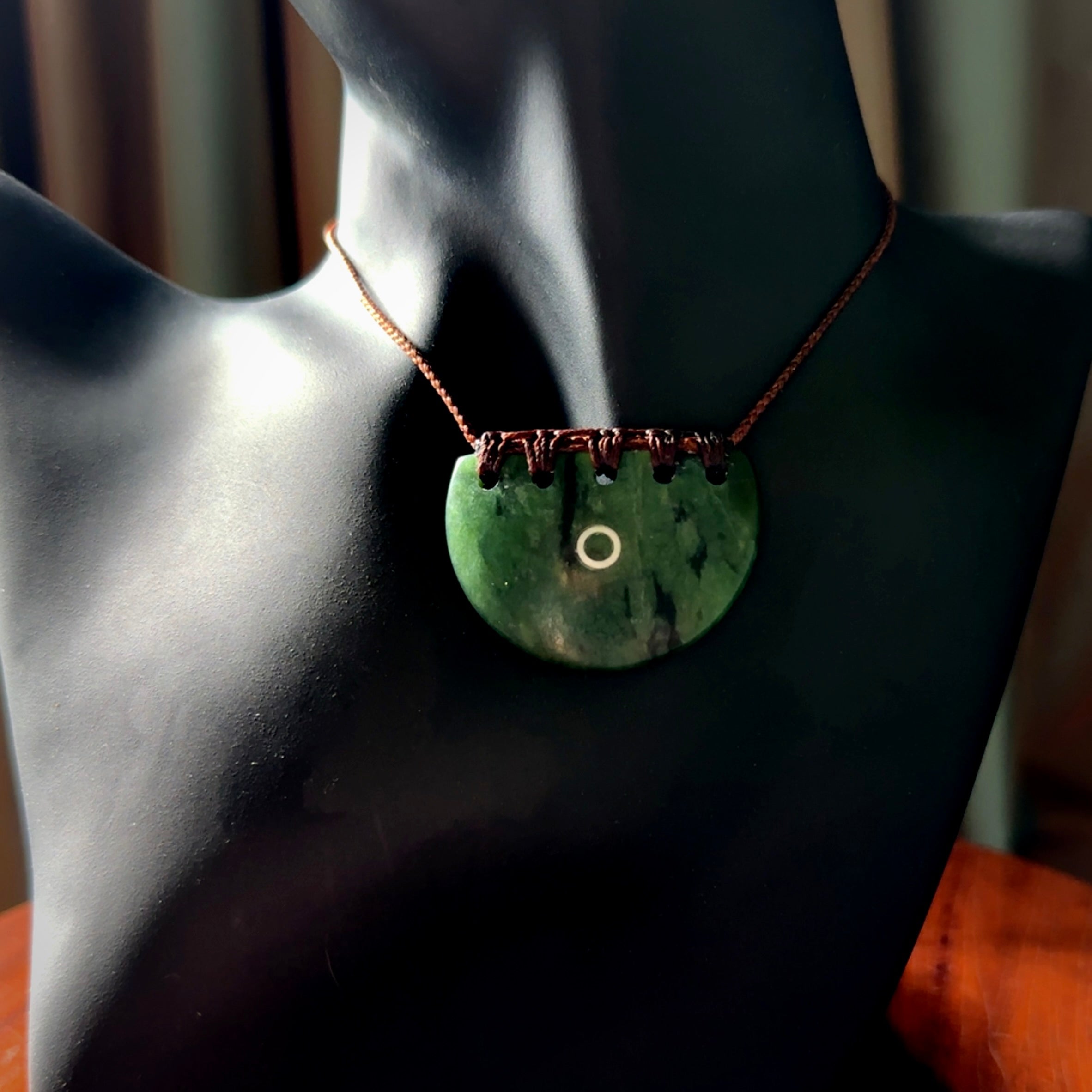 This picture shows a small hand carved jade contemporary half-shield pendant with whale tooth inlay. It is a deep green and is a wonderful, delicate piece of jewellery. The cord is hand plaited and adjustable so that you can position the pendant where it suits you best. This piece was carved for us by Kyohei Noguchi. Delivery is free worldwide.