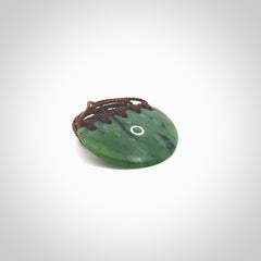 This picture shows a small hand carved jade contemporary half-shield pendant with whale tooth inlay. It is a deep green and is a wonderful, delicate piece of jewellery. The cord is hand plaited and adjustable so that you can position the pendant where it suits you best. This piece was carved for us by Kyohei Noguchi. Delivery is free worldwide.