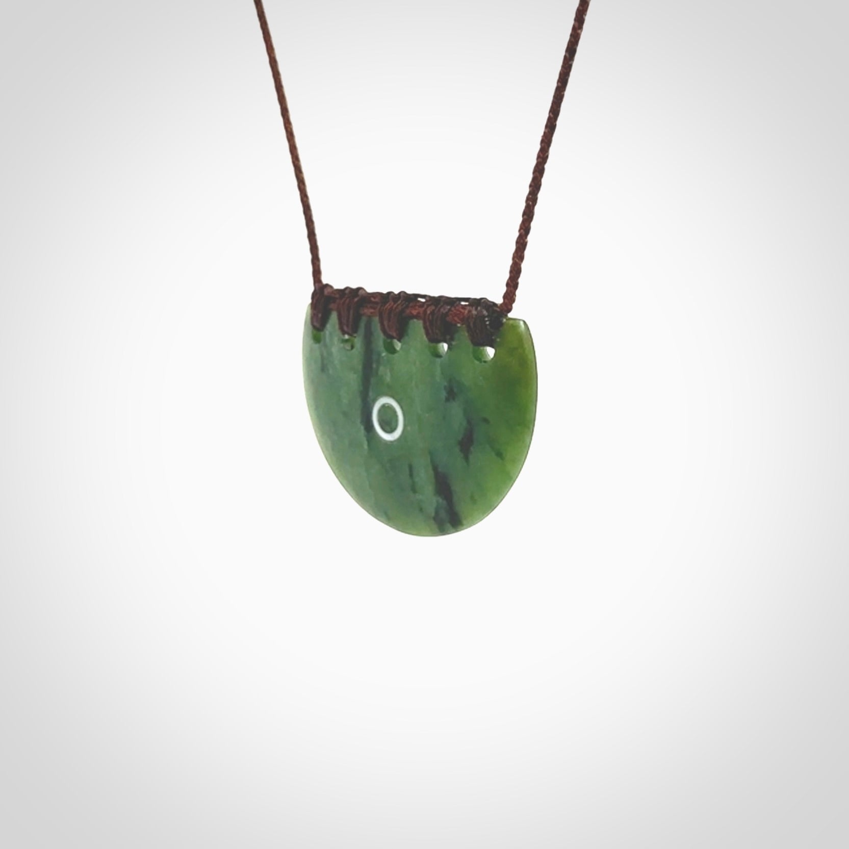 This picture shows a small hand carved jade contemporary half-shield pendant with whale tooth inlay. It is a deep green and is a wonderful, delicate piece of jewellery. The cord is hand plaited and adjustable so that you can position the pendant where it suits you best. This piece was carved for us by Kyohei Noguchi. Delivery is free worldwide.