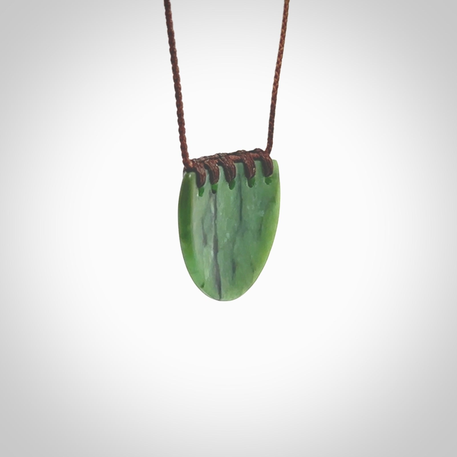 This picture shows a small hand carved jade contemporary half-shield pendant with whale tooth inlay. It is a deep green and is a wonderful, delicate piece of jewellery. The cord is hand plaited and adjustable so that you can position the pendant where it suits you best. This piece was carved for us by Kyohei Noguchi. Delivery is free worldwide.