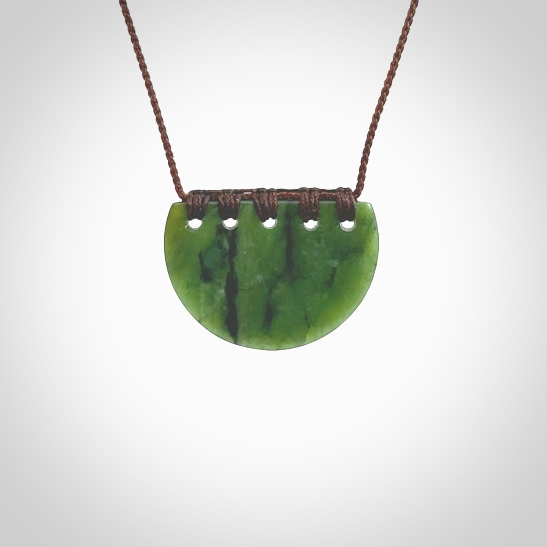 This picture shows a small hand carved jade contemporary half-shield pendant with whale tooth inlay. It is a deep green and is a wonderful, delicate piece of jewellery. The cord is hand plaited and adjustable so that you can position the pendant where it suits you best. This piece was carved for us by Kyohei Noguchi. Delivery is free worldwide.