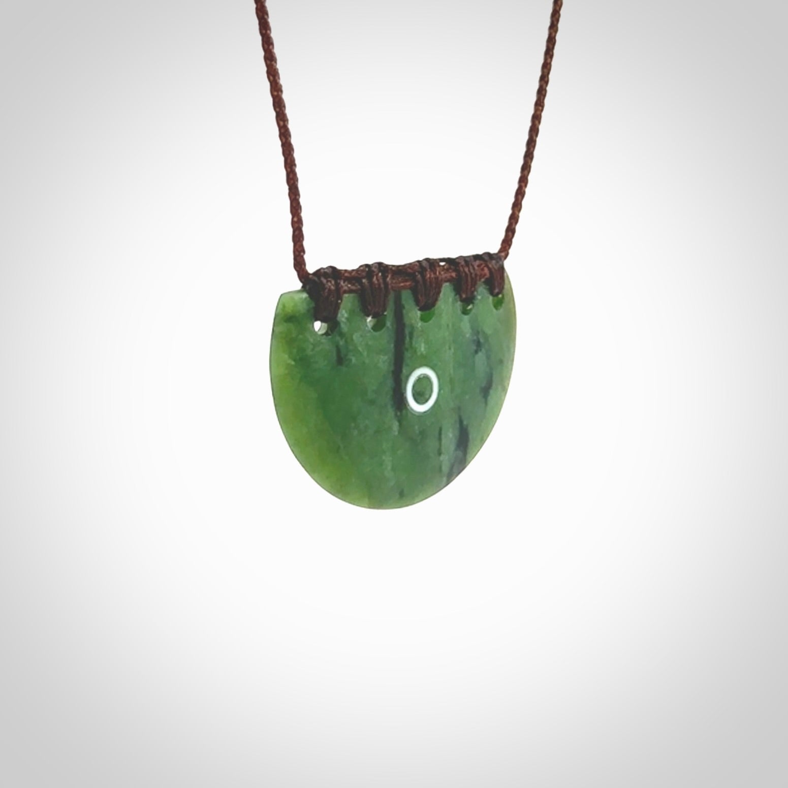 This picture shows a small hand carved jade contemporary half-shield pendant with whale tooth inlay. It is a deep green and is a wonderful, delicate piece of jewellery. The cord is hand plaited and adjustable so that you can position the pendant where it suits you best. This piece was carved for us by Kyohei Noguchi. Delivery is free worldwide.