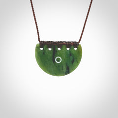 This picture shows a small hand carved jade contemporary half-shield pendant with whale tooth inlay. It is a deep green and is a wonderful, delicate piece of jewellery. The cord is hand plaited and adjustable so that you can position the pendant where it suits you best. This piece was carved for us by Kyohei Noguchi. Delivery is free worldwide.