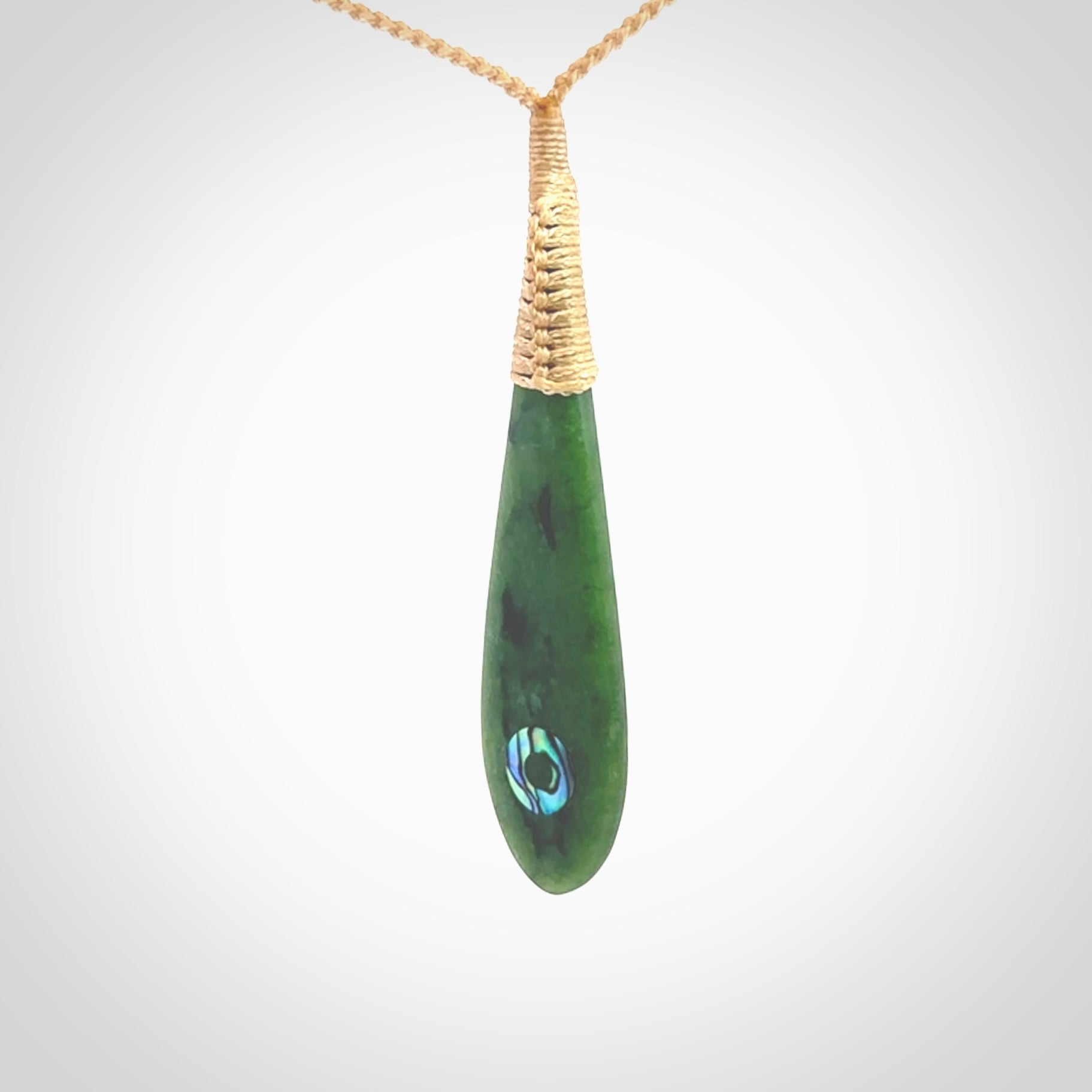 This photo shows a beautiful jade drop with paua shell inlay. It is hand carved from a piece of green New Zealand pounamu, with fascinating light green inclusions throughout the stone. We have this on a beige coloured, adjustable four plait cord. We ship this worldwide with an express courier service. Postage is free.