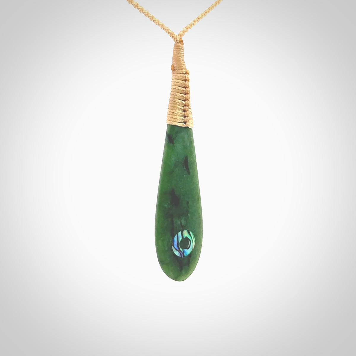 This photo shows a beautiful jade drop with paua shell inlay. It is hand carved from a piece of green New Zealand pounamu, with fascinating light green inclusions throughout the stone. We have this on a beige coloured, adjustable four plait cord. We ship this worldwide with an express courier service. Postage is free.