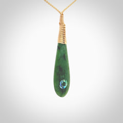 This photo shows a beautiful jade drop with paua shell inlay. It is hand carved from a piece of green New Zealand pounamu, with fascinating light green inclusions throughout the stone. We have this on a beige coloured, adjustable four plait cord. We ship this worldwide with an express courier service. Postage is free.