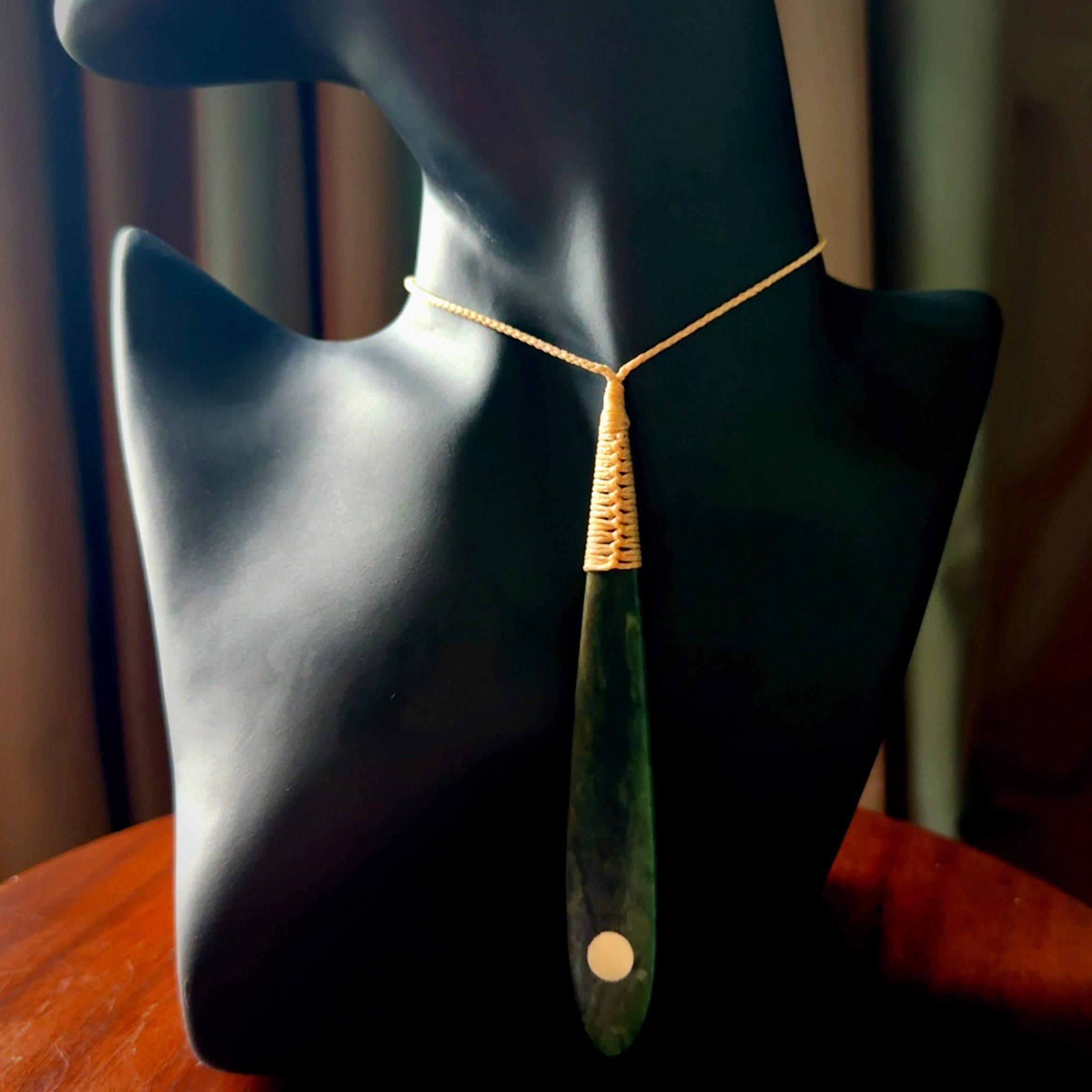 This photo shows a large beautiful jade drop with whale tooth inlay. It is hand carved from a piece of green New Zealand pounamu, with fascinating light green inclusions throughout the stone. We have this on a beige coloured, adjustable four plait cord. We ship this worldwide with an express courier service. Postage is free.