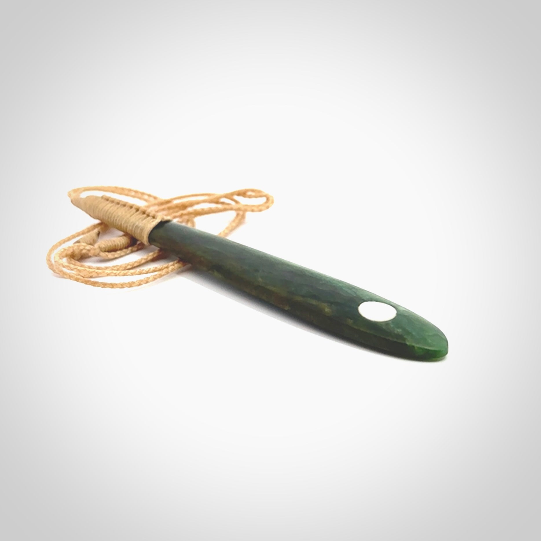 This photo shows a large beautiful jade drop with whale tooth inlay. It is hand carved from a piece of green New Zealand pounamu, with fascinating light green inclusions throughout the stone. We have this on a beige coloured, adjustable four plait cord. We ship this worldwide with an express courier service. Postage is free.