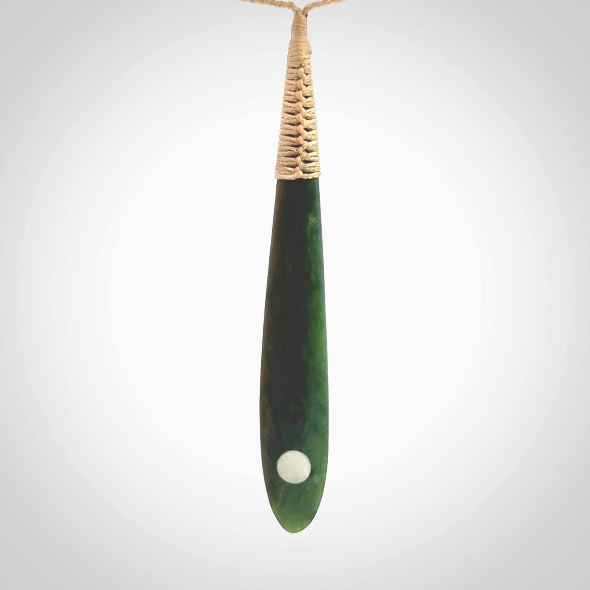 This photo shows a large beautiful jade drop with whale tooth inlay. It is hand carved from a piece of green New Zealand pounamu, with fascinating light green inclusions throughout the stone. We have this on a beige coloured, adjustable four plait cord. We ship this worldwide with an express courier service. Postage is free.