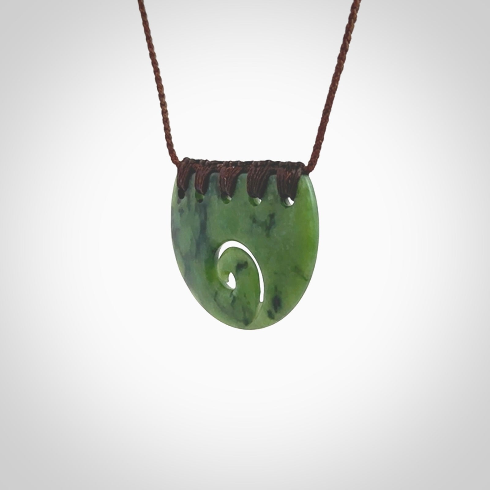 This picture shows a small hand carved jade contemporary half-shield pendant with koru heart. It is a deep green and is a wonderful, delicate piece of jewellery. The cord is hand plaited and adjustable so that you can position the pendant where it suits you best. This piece was carved for us by Kyohei Noguchi. Delivery is free worldwide.