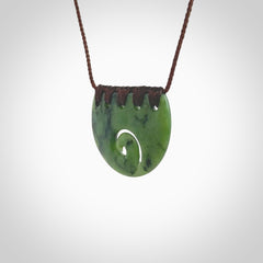 This picture shows a small hand carved jade contemporary half-shield pendant with koru heart. It is a deep green and is a wonderful, delicate piece of jewellery. The cord is hand plaited and adjustable so that you can position the pendant where it suits you best. This piece was carved for us by Kyohei Noguchi. Delivery is free worldwide.