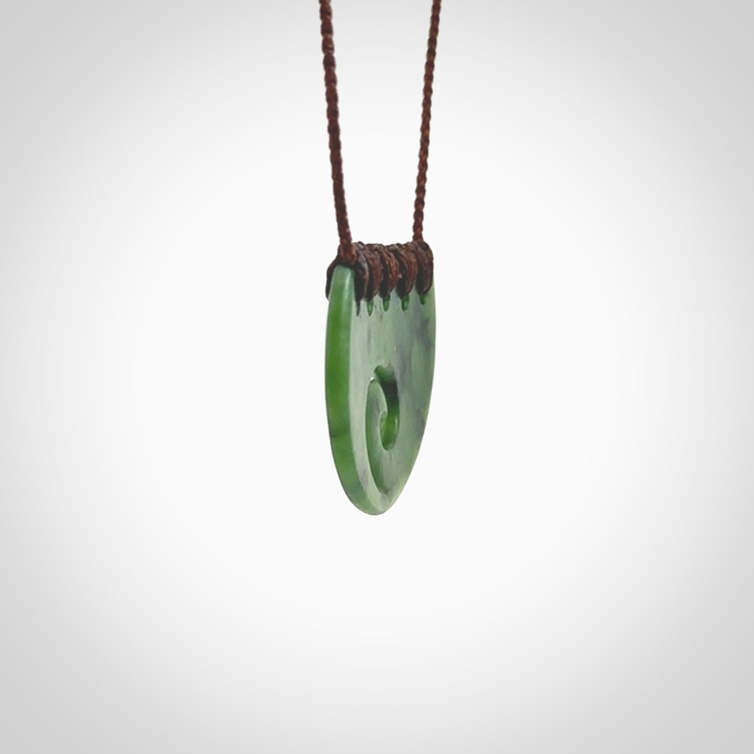 This picture shows a small hand carved jade contemporary half-shield pendant with koru heart. It is a deep green and is a wonderful, delicate piece of jewellery. The cord is hand plaited and adjustable so that you can position the pendant where it suits you best. This piece was carved for us by Kyohei Noguchi. Delivery is free worldwide.