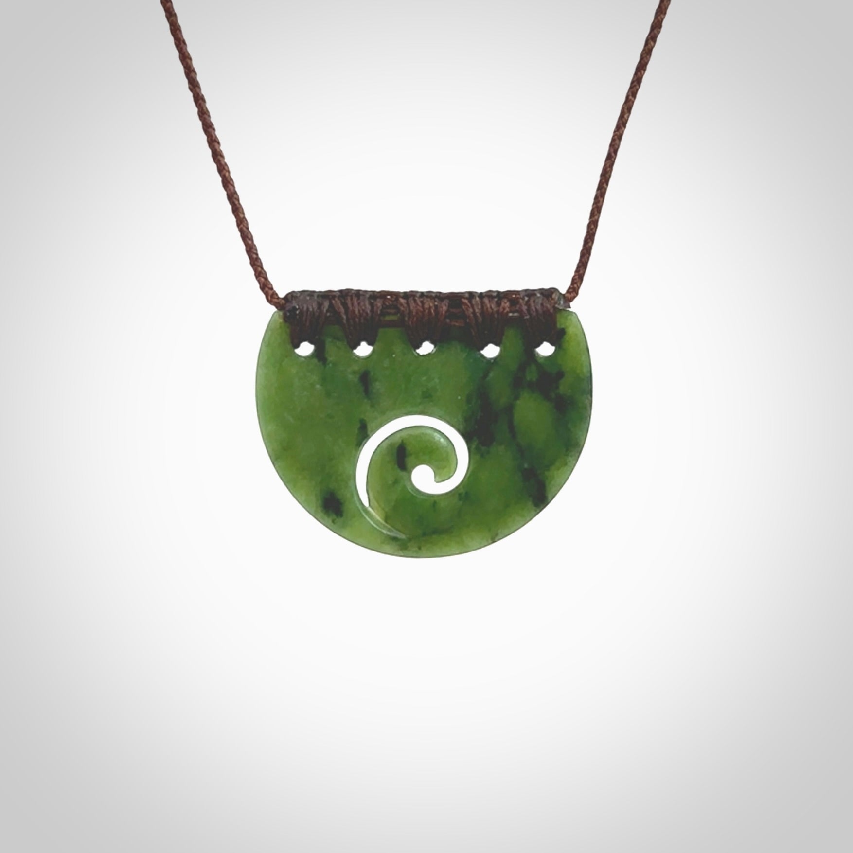 This picture shows a small hand carved jade contemporary half-shield pendant with koru heart. It is a deep green and is a wonderful, delicate piece of jewellery. The cord is hand plaited and adjustable so that you can position the pendant where it suits you best. This piece was carved for us by Kyohei Noguchi. Delivery is free worldwide.