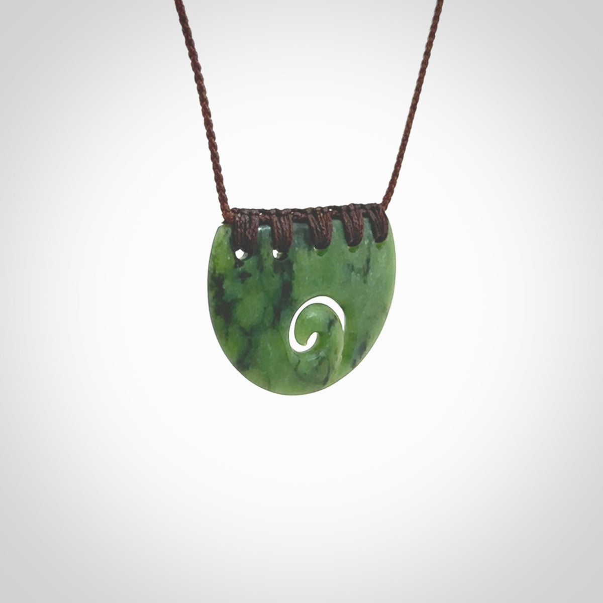 This picture shows a small hand carved jade contemporary half-shield pendant with koru heart. It is a deep green and is a wonderful, delicate piece of jewellery. The cord is hand plaited and adjustable so that you can position the pendant where it suits you best. This piece was carved for us by Kyohei Noguchi. Delivery is free worldwide.